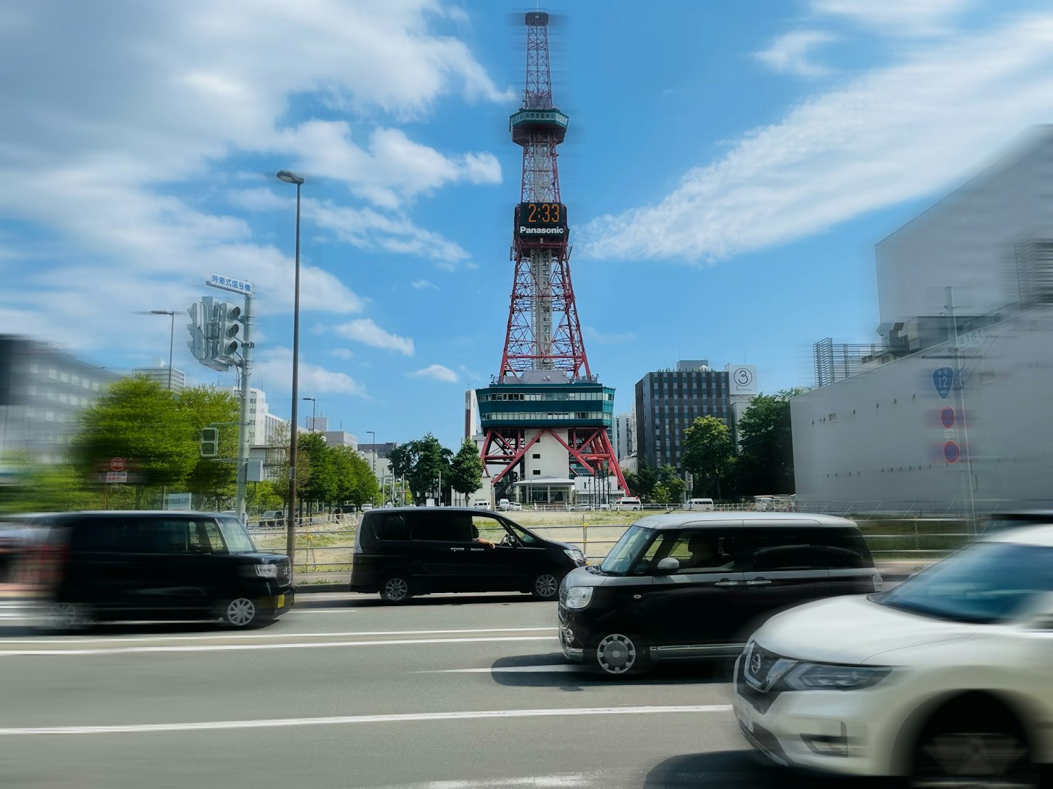 Tháp truyền hình Nagoya đứng dưới bầu trời xanh với những chiếc xe đi qua