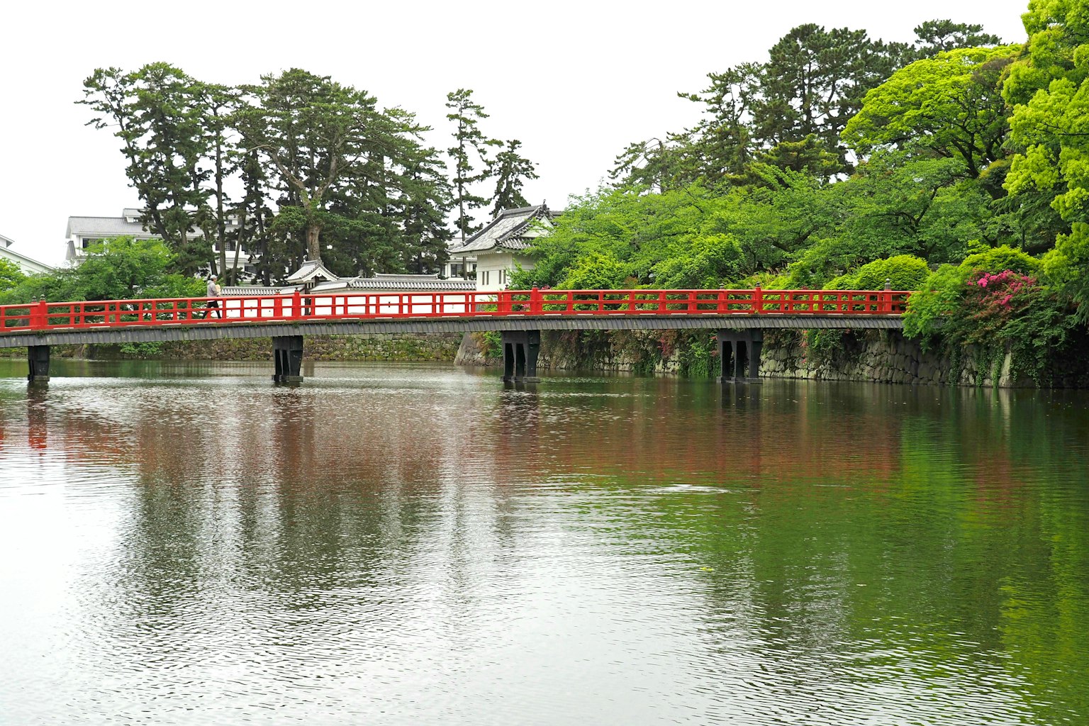 ทิวทัศน์ของบ่อน้ำสงบที่มีสะพานสีแดงสะท้อนอยู่ในน้ำ