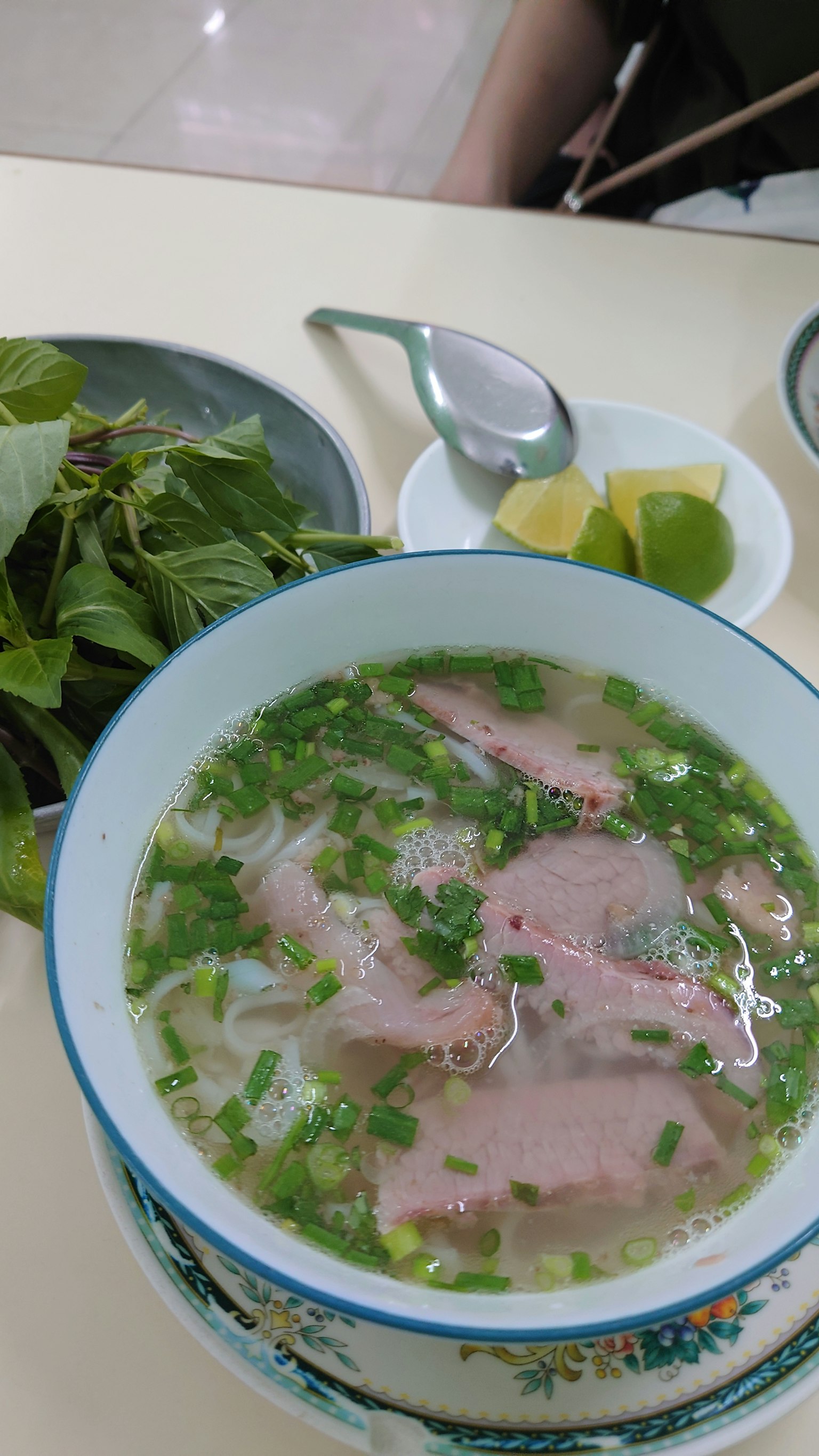 Mangkok pho dengan herba hijau dan jeruk nipis di samping