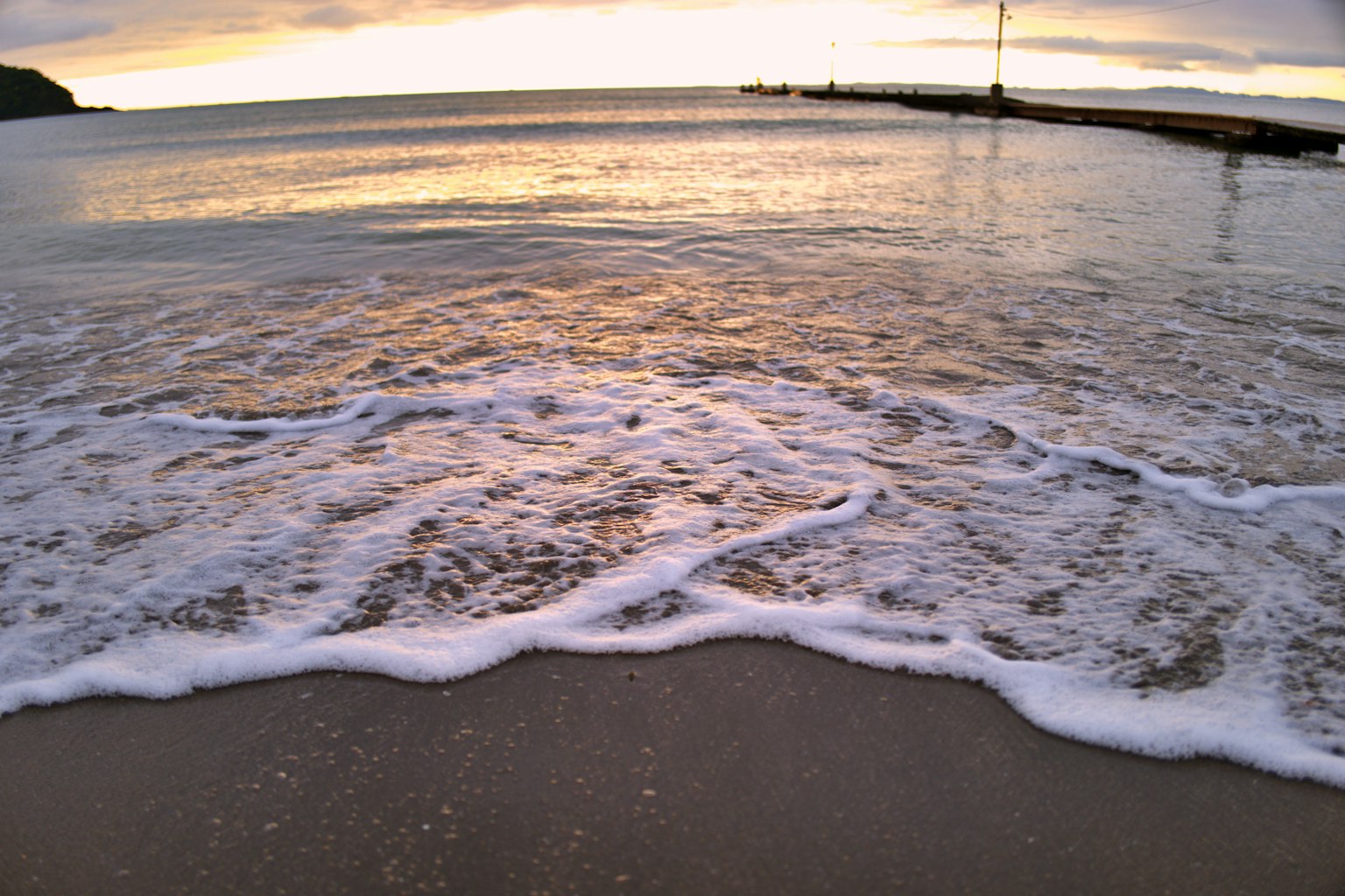 Ruhiges Meer mit Wellen, die am Sandstrand bei Sonnenuntergang brechen