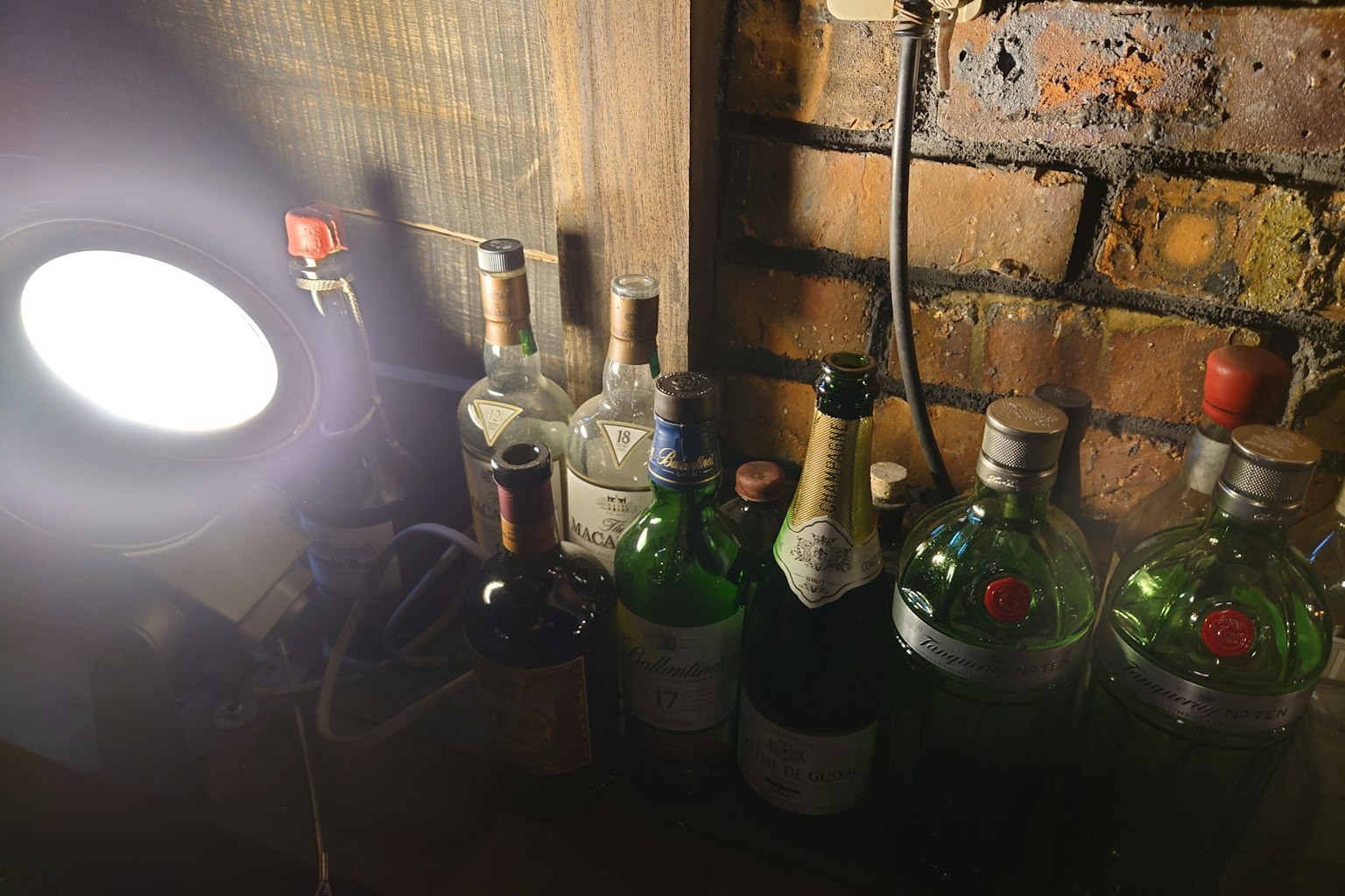 Imagen de varias botellas de licor y una lámpara cerca de una pared de madera