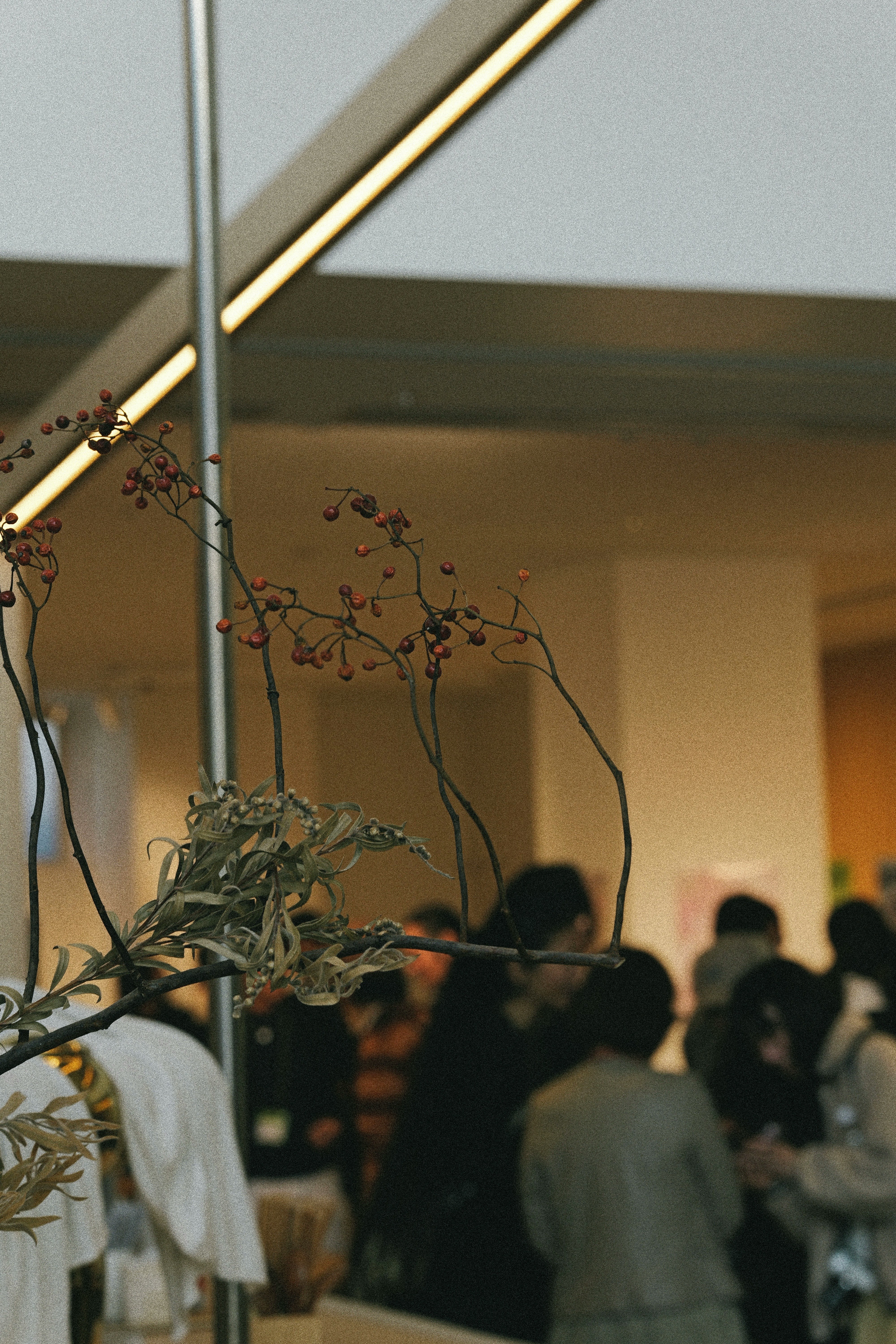 花の枝と会場の人影が見える展示空間の室内風景