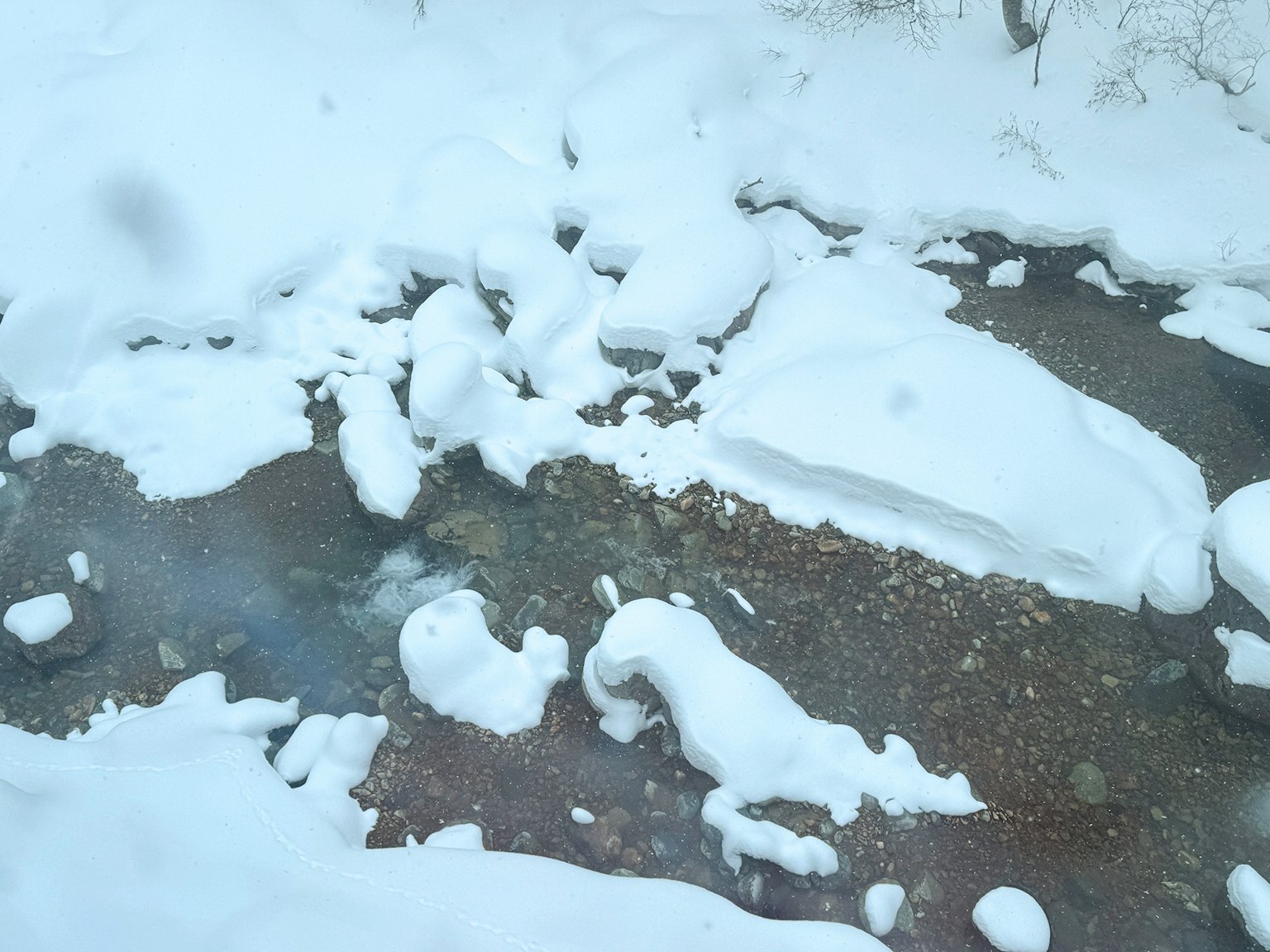 Un paesaggio innevato con un ruscello visibile con rocce e acqua