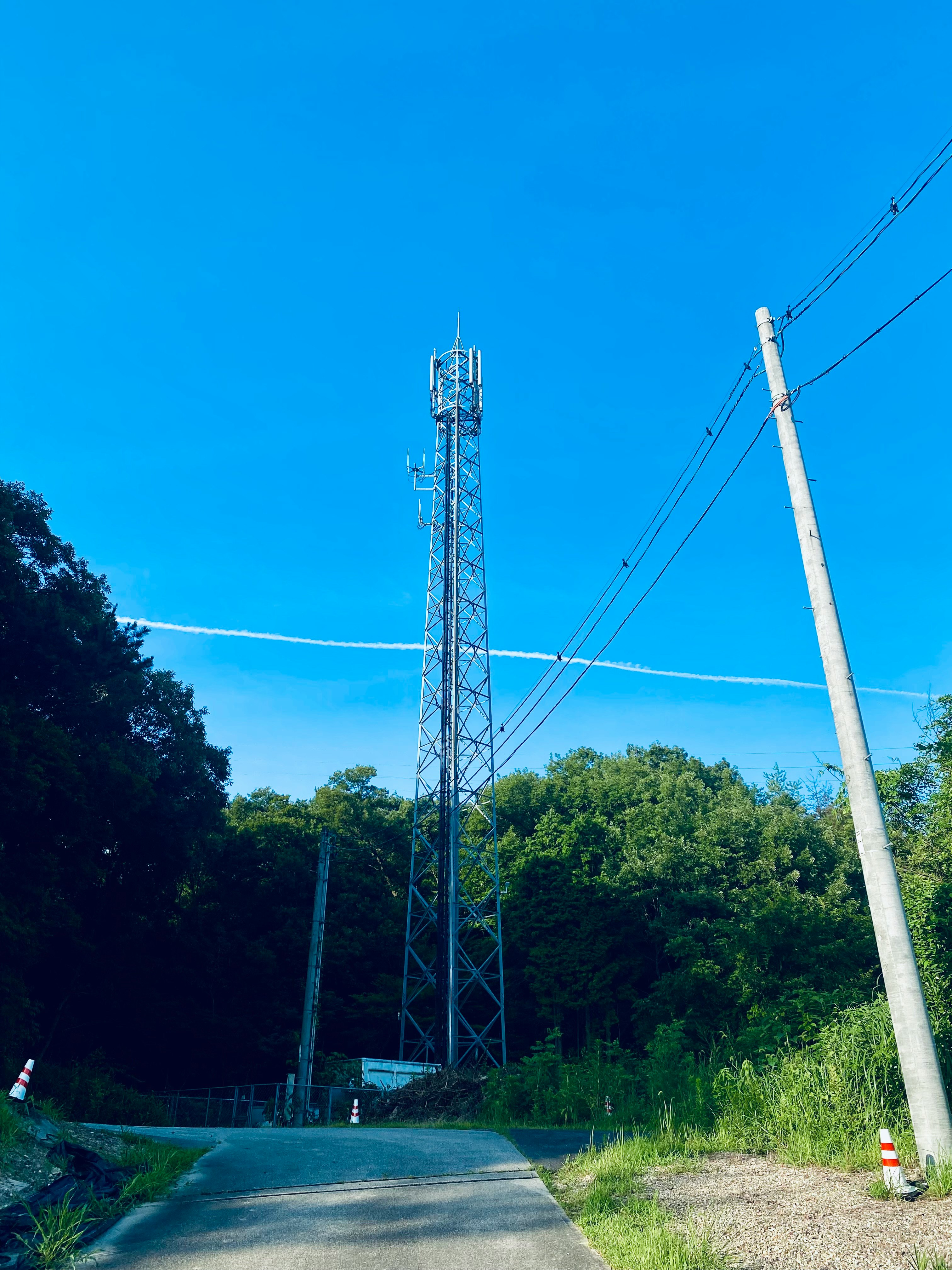 青空の下に立つ電波塔と送電線のある工業的な鉄塔