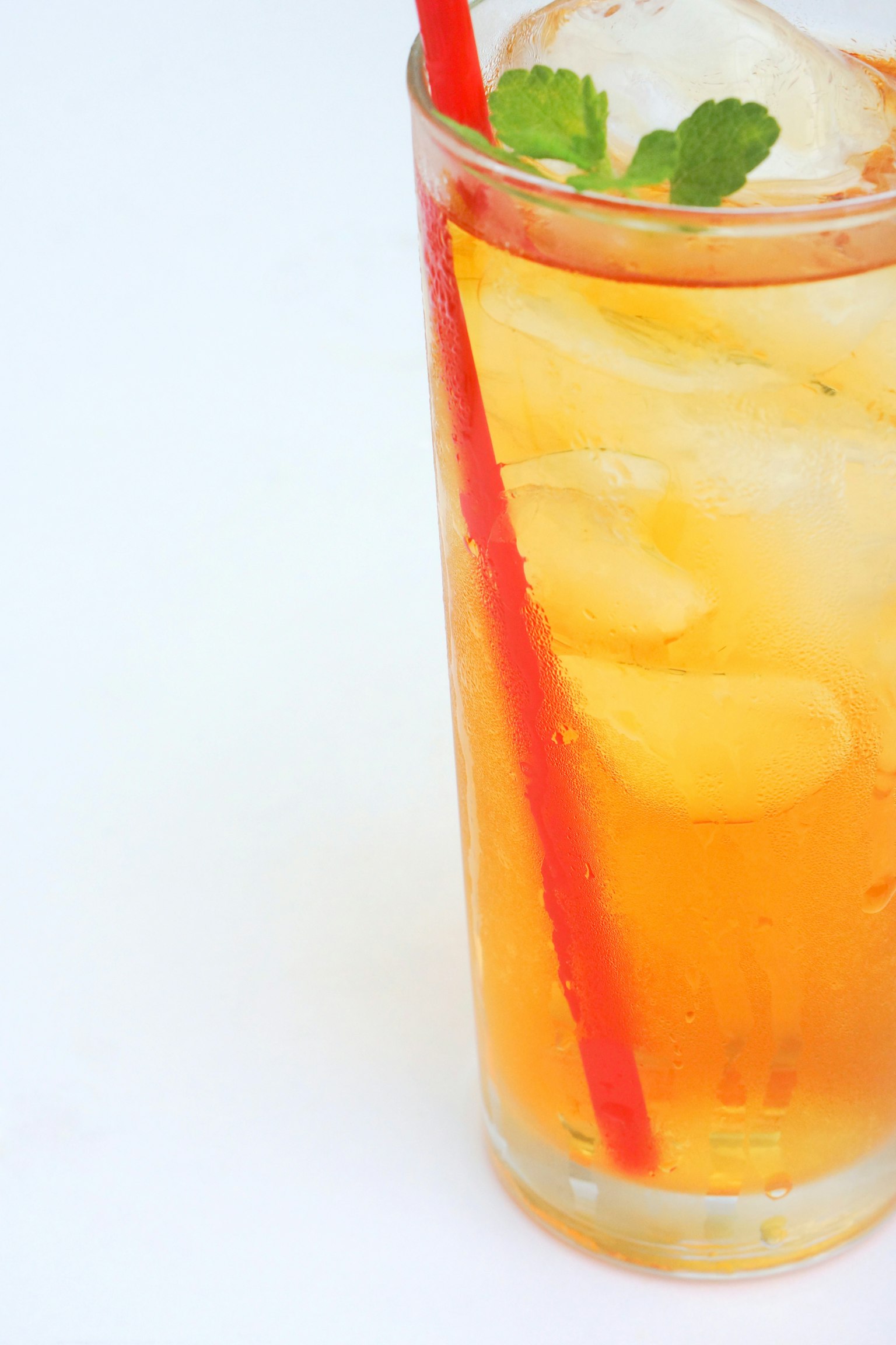 Tè freddo in un bicchiere trasparente con una cannuccia rossa e una foglia di menta