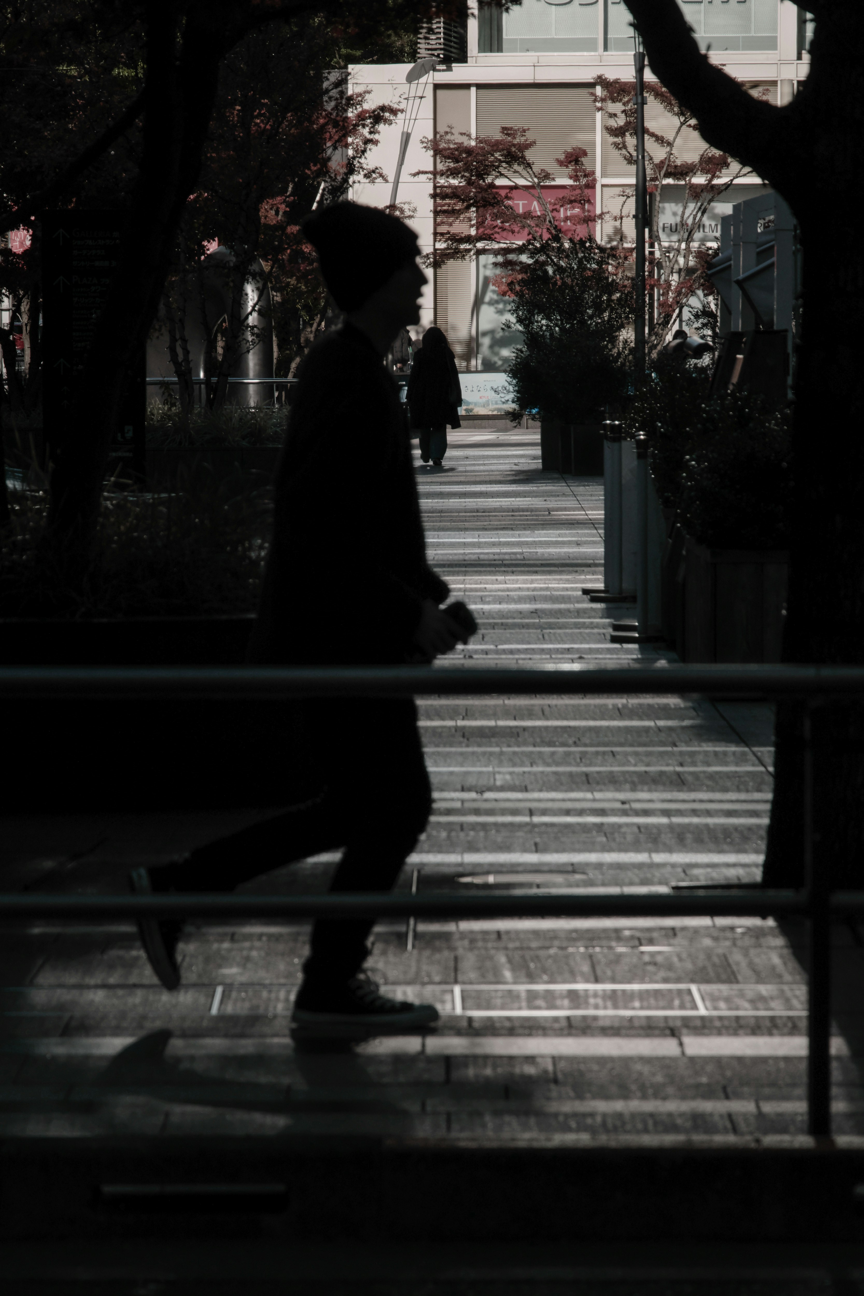 朝の街路を歩く人影とベンチのある通り