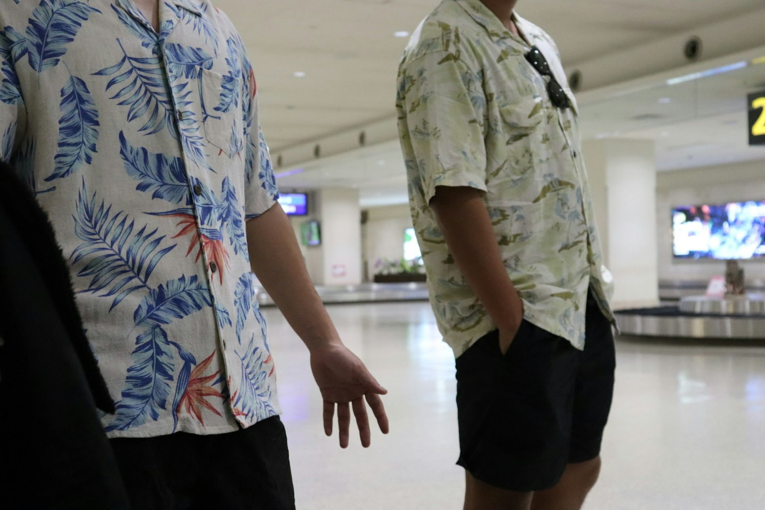 Two men waiting at the airport baggage claim wearing tropical patterned shirts