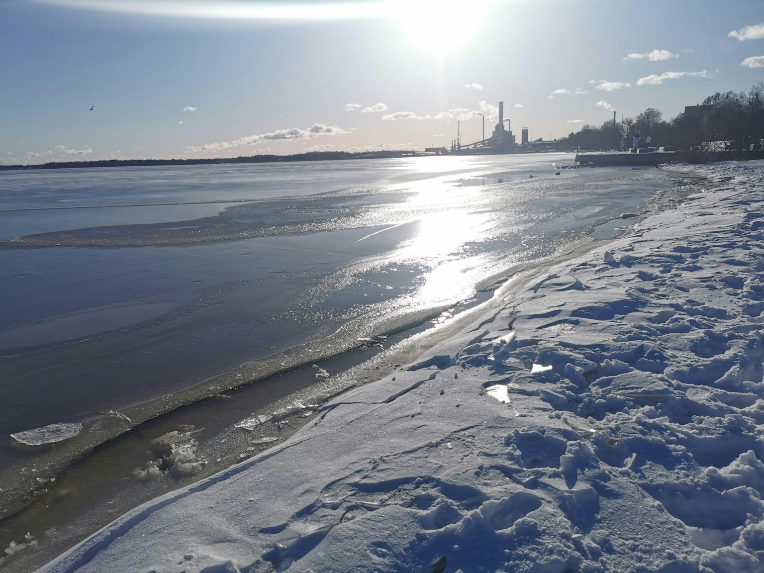 Garis pantai yang tertutup salju dengan danau beku dan air yang diterangi matahari