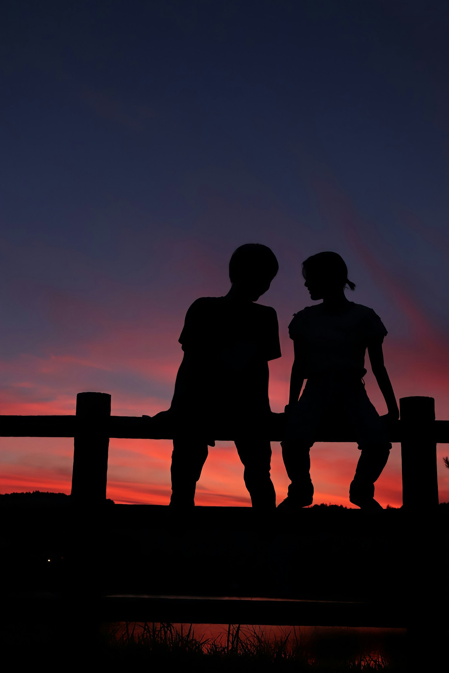 일몰 중 난간에 앉아 있는 실루엣의 커플