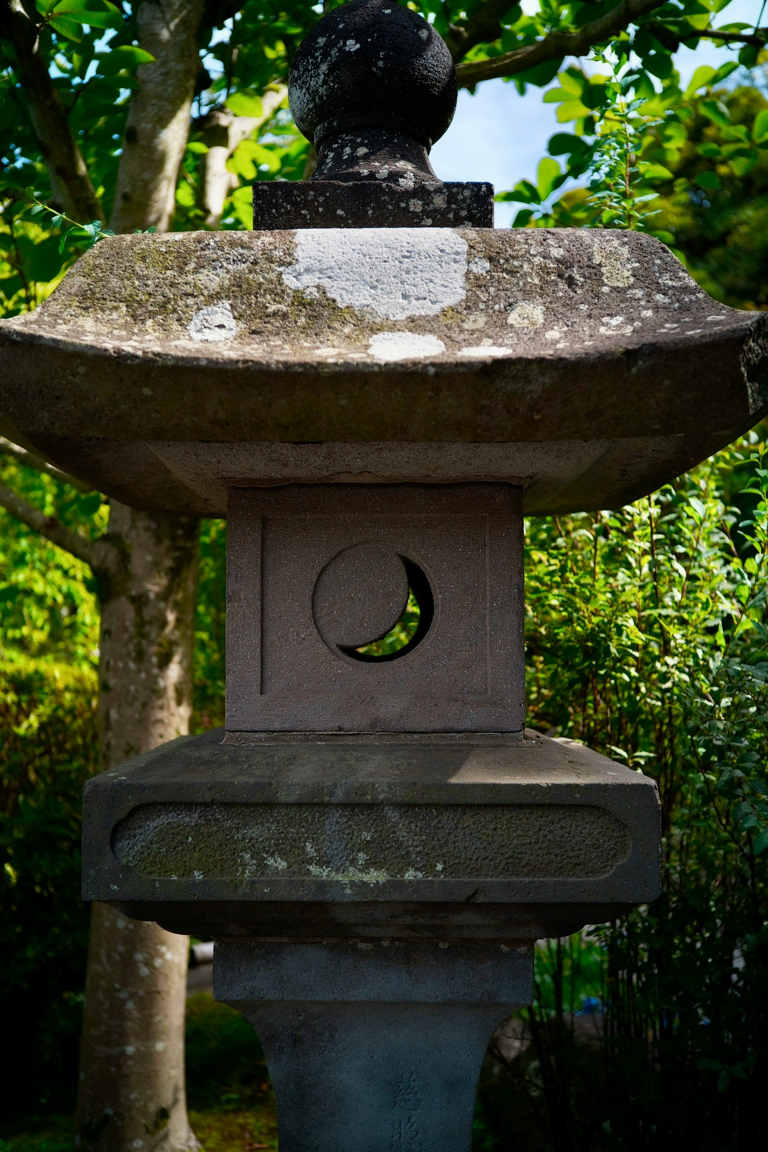 ภาพระยะใกล้ของโคมไฟหินที่ล้อมรอบด้วยต้นไม้สีเขียวแสดงให้เห็นลักษณะการออกแบบที่เป็นเอกลักษณ์