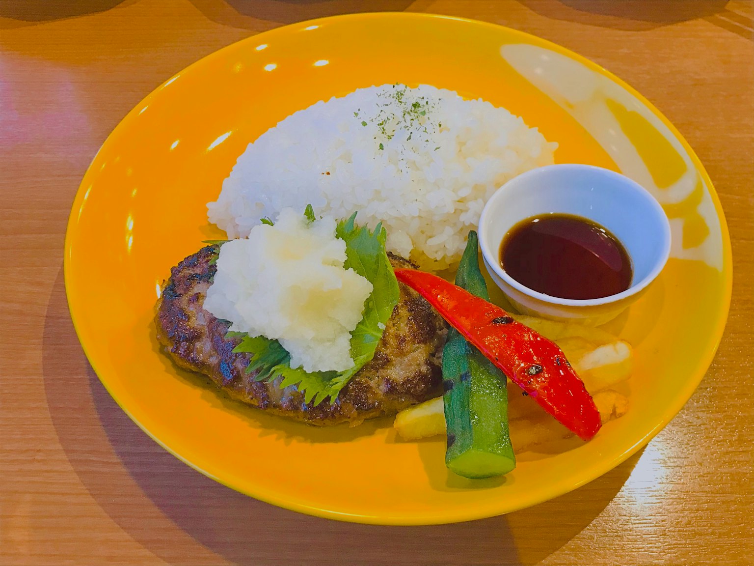 A plate with rice, grilled meat, vegetables, and dipping sauce