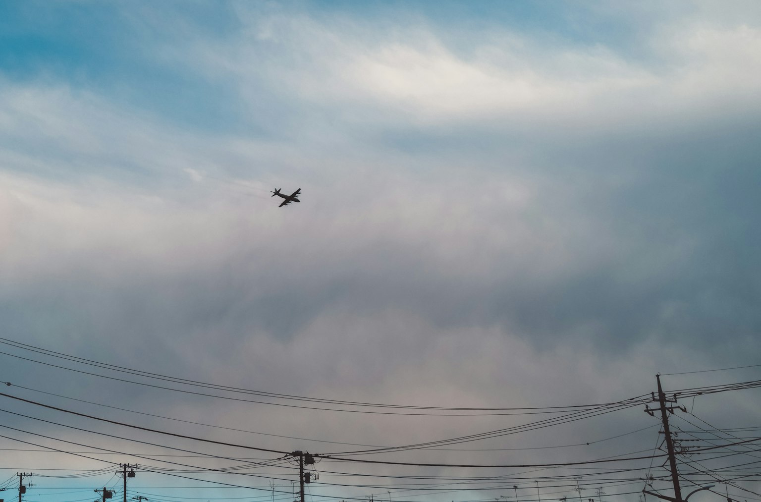 Sebuah pesawat terbang di atas awan dan kabel listrik