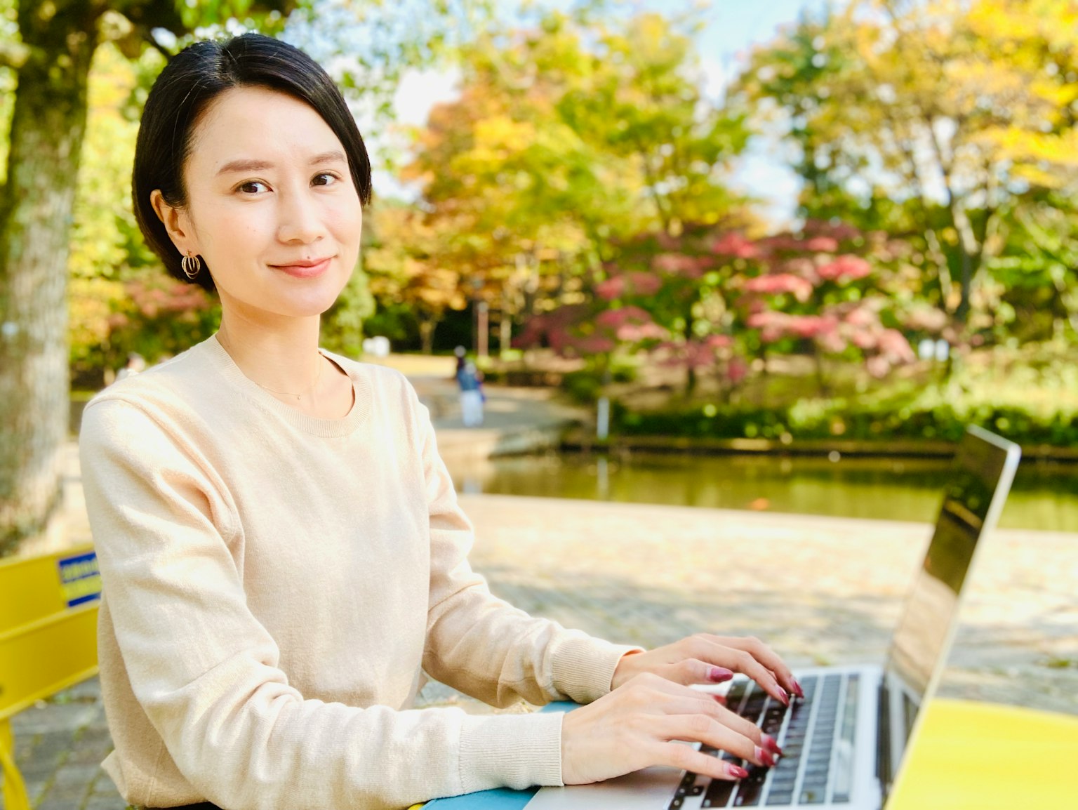 Porträt einer Frau, die in einem Park mit bunten Bäumen im Hintergrund einen Laptop benutzt