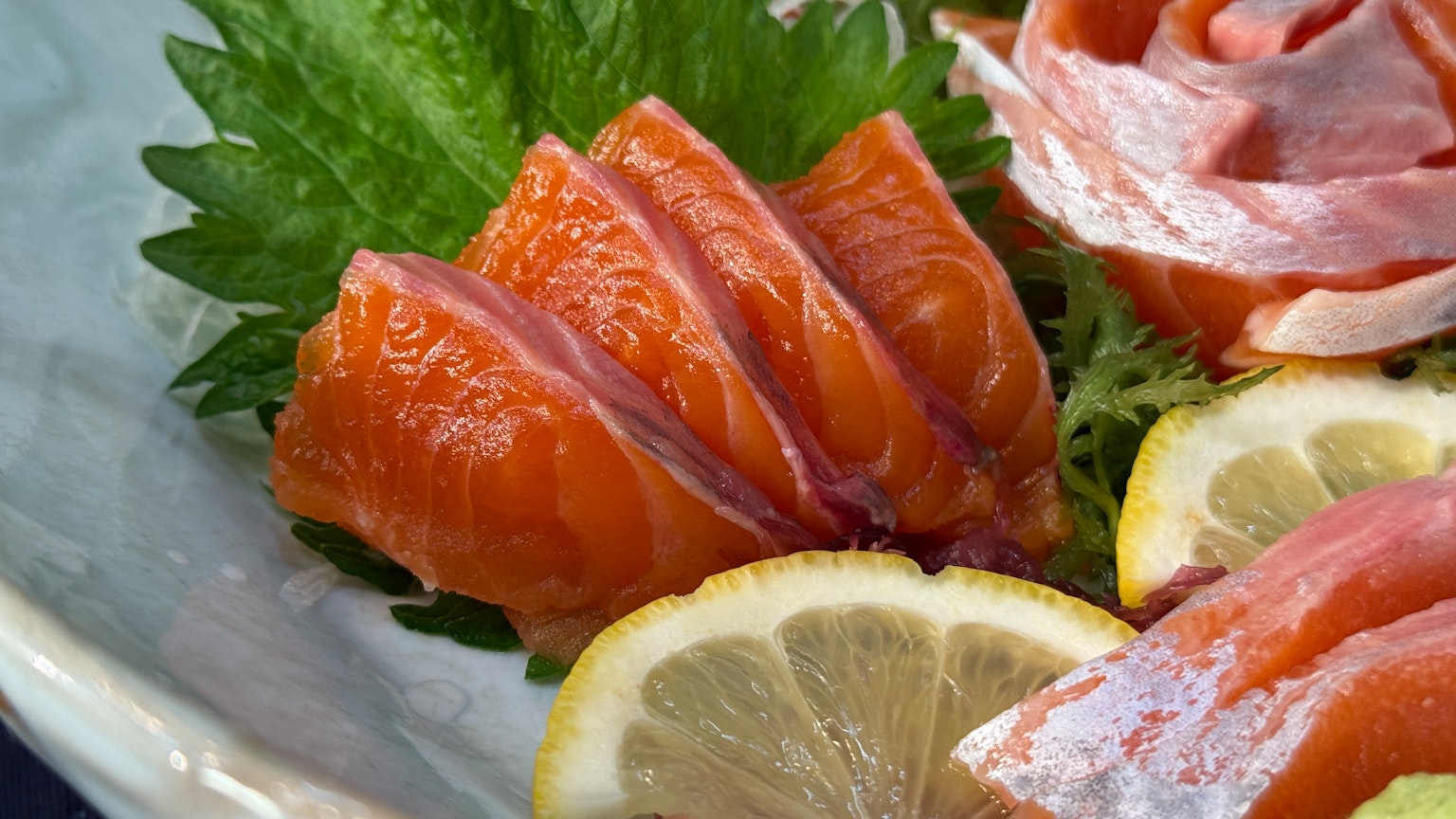 Lebendige Scheiben von Lachs-Sashimi, begleitet von Zitronenscheiben auf einem Teller