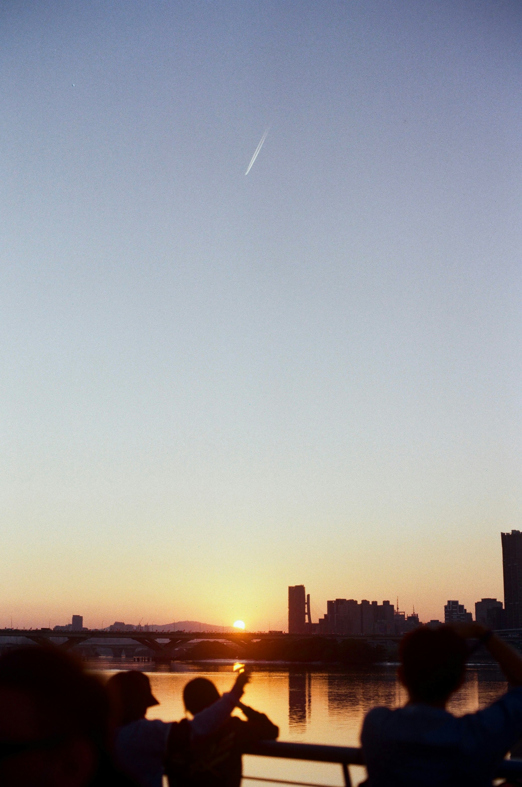夕暮れの川沿いで見上げる人々のシルエット