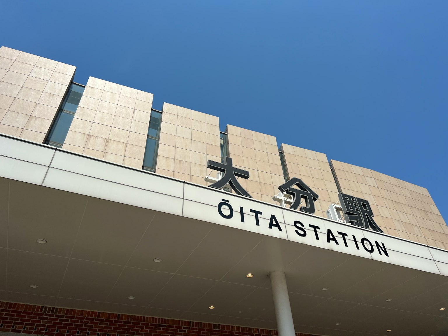 Insegna della stazione di Oita visibile sotto un cielo blu