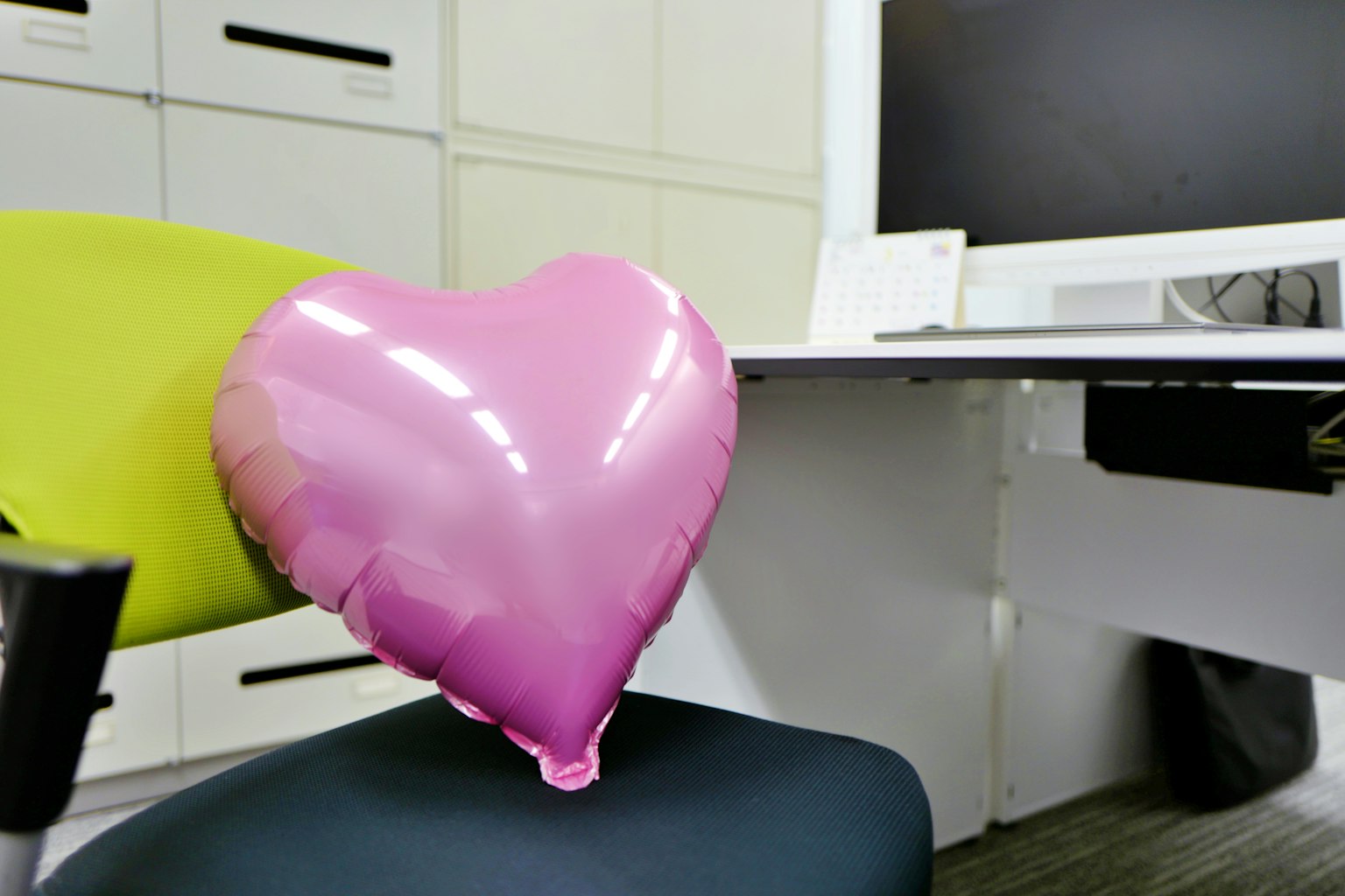 Pallone a forma di cuore rosa appoggiato su una sedia verde in un ambiente d'ufficio