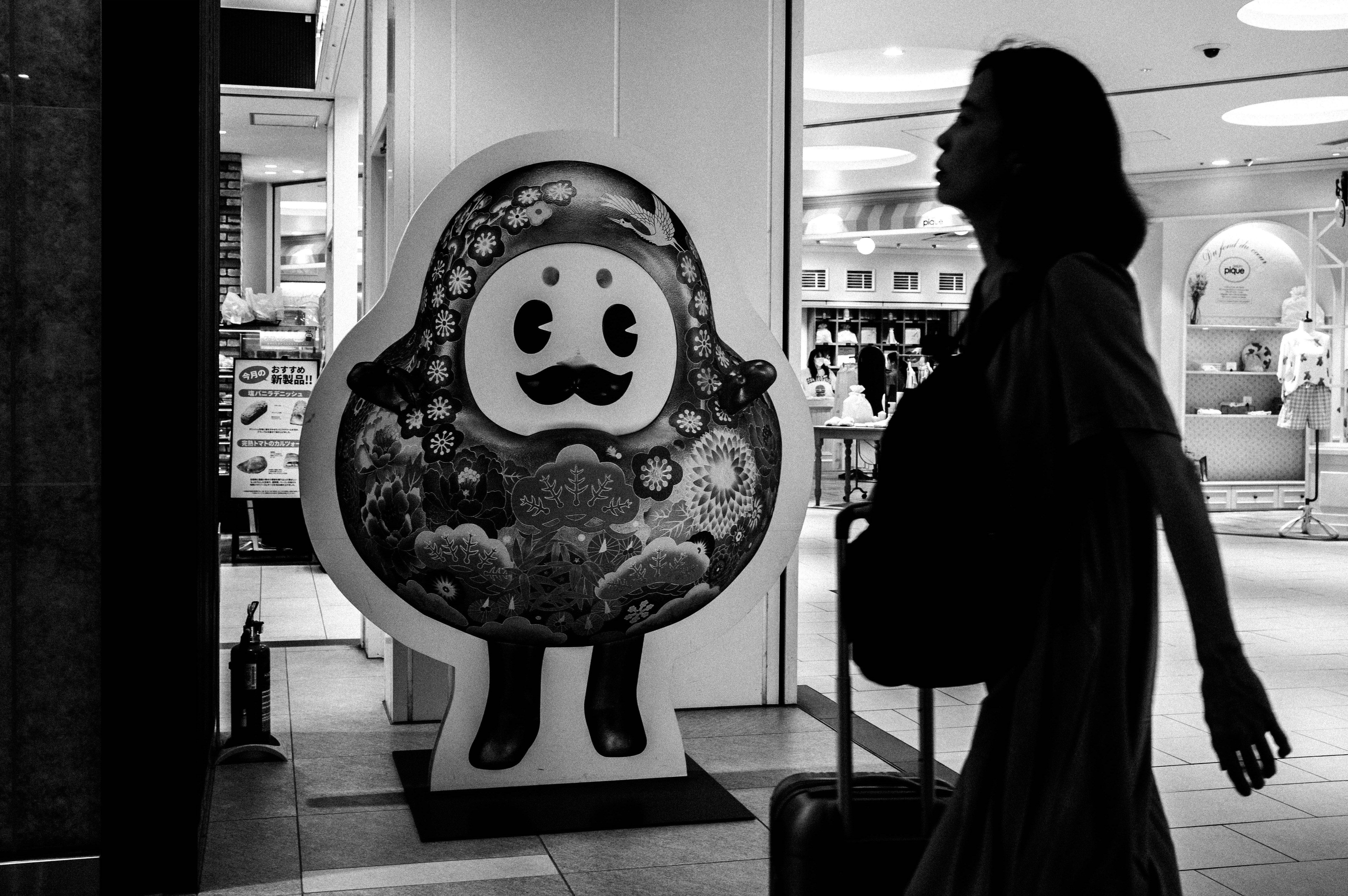Black-and-white silhouette of a person walking past a character figure inside a store