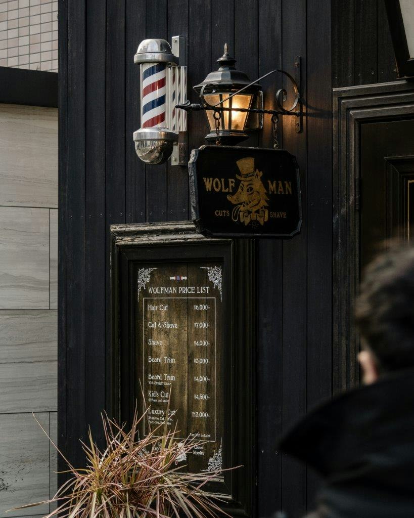 Entrada con un letrero colgado y una linterna en una pared exterior oscura