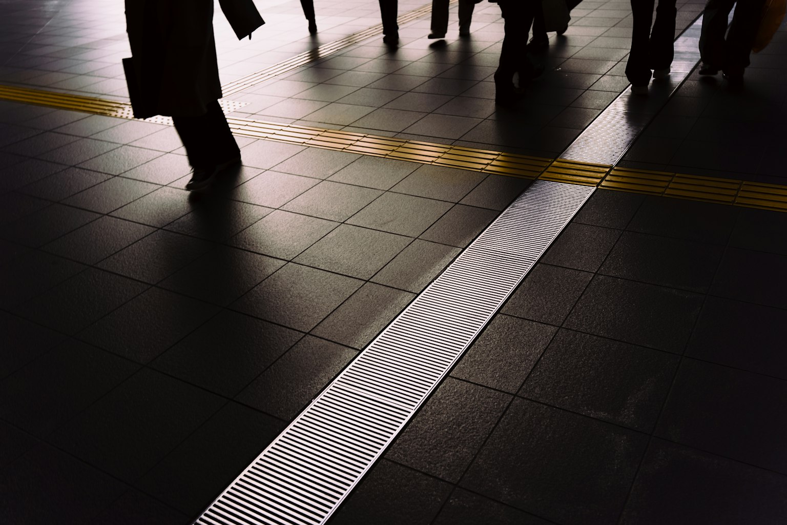 Des personnes marchant sur le sol d'une station avec une ligne guide blanche et une ligne jaune