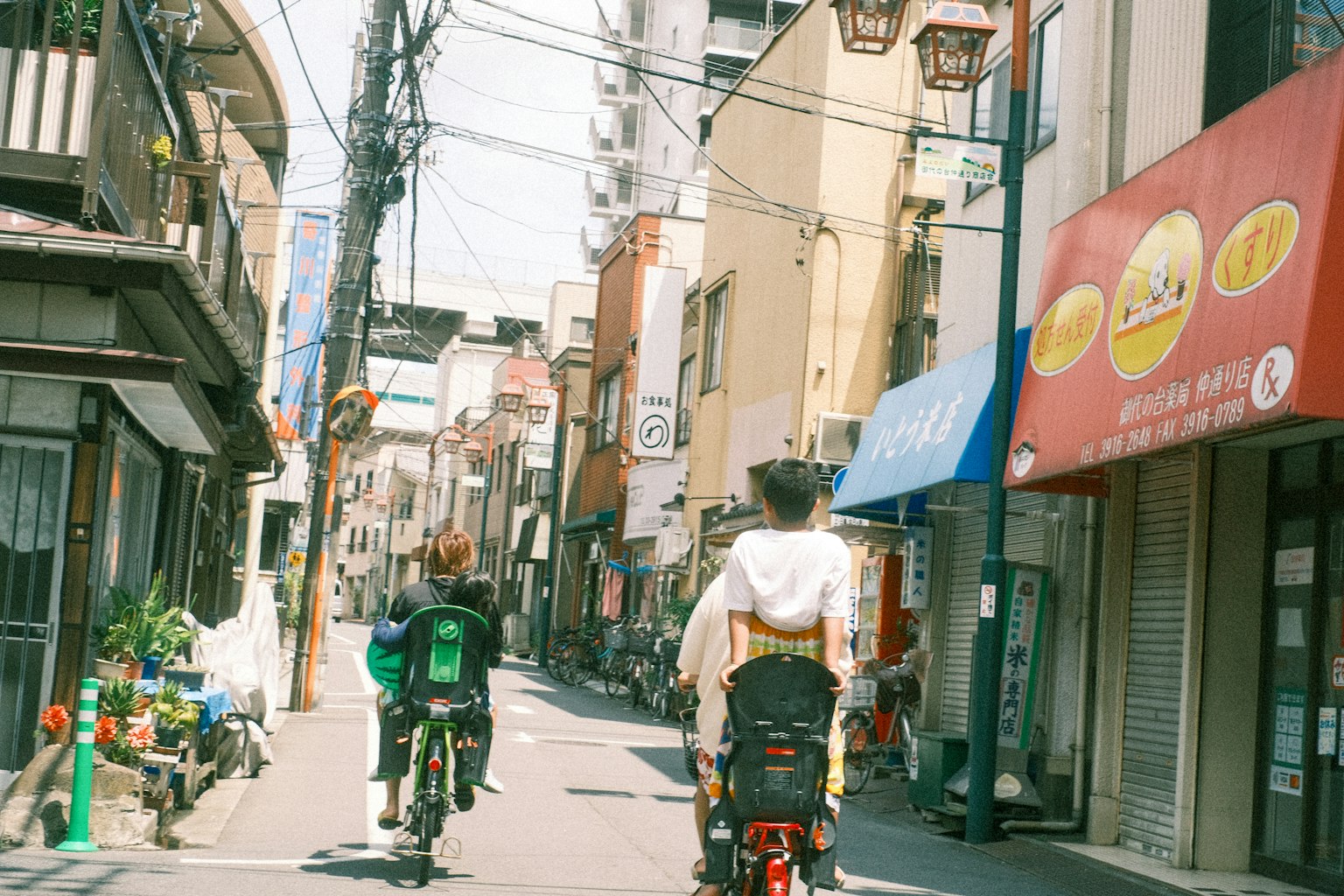 Hai người đi xe đạp trên một con phố hẹp với những tòa nhà cổ và dây điện