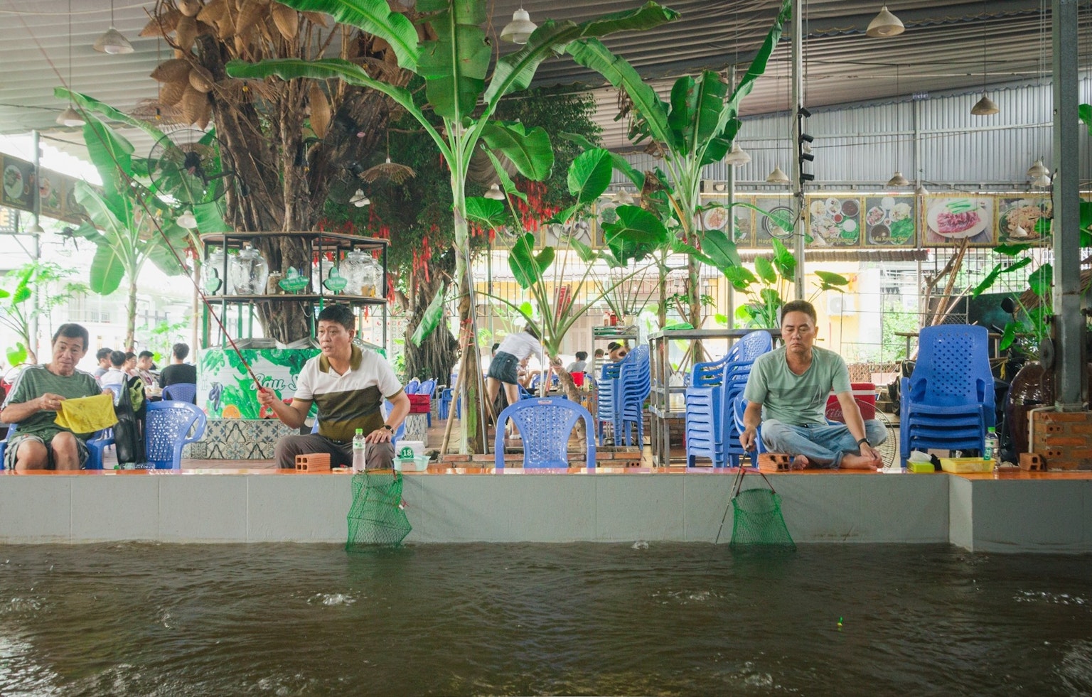 People sitting by the water indoors surrounded by green plants