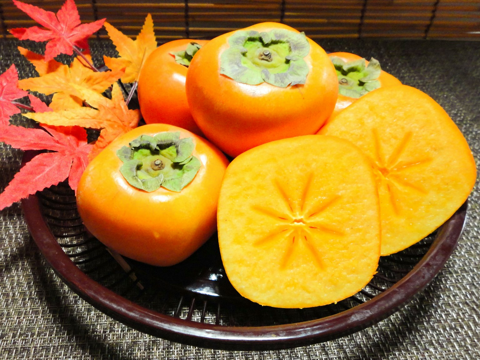 Un plato de caquis naranjas con hojas de otoño