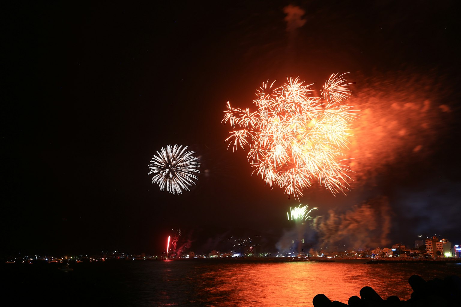 Fuochi d'artificio colorati che esplodono nel cielo notturno riflessi sull'acqua