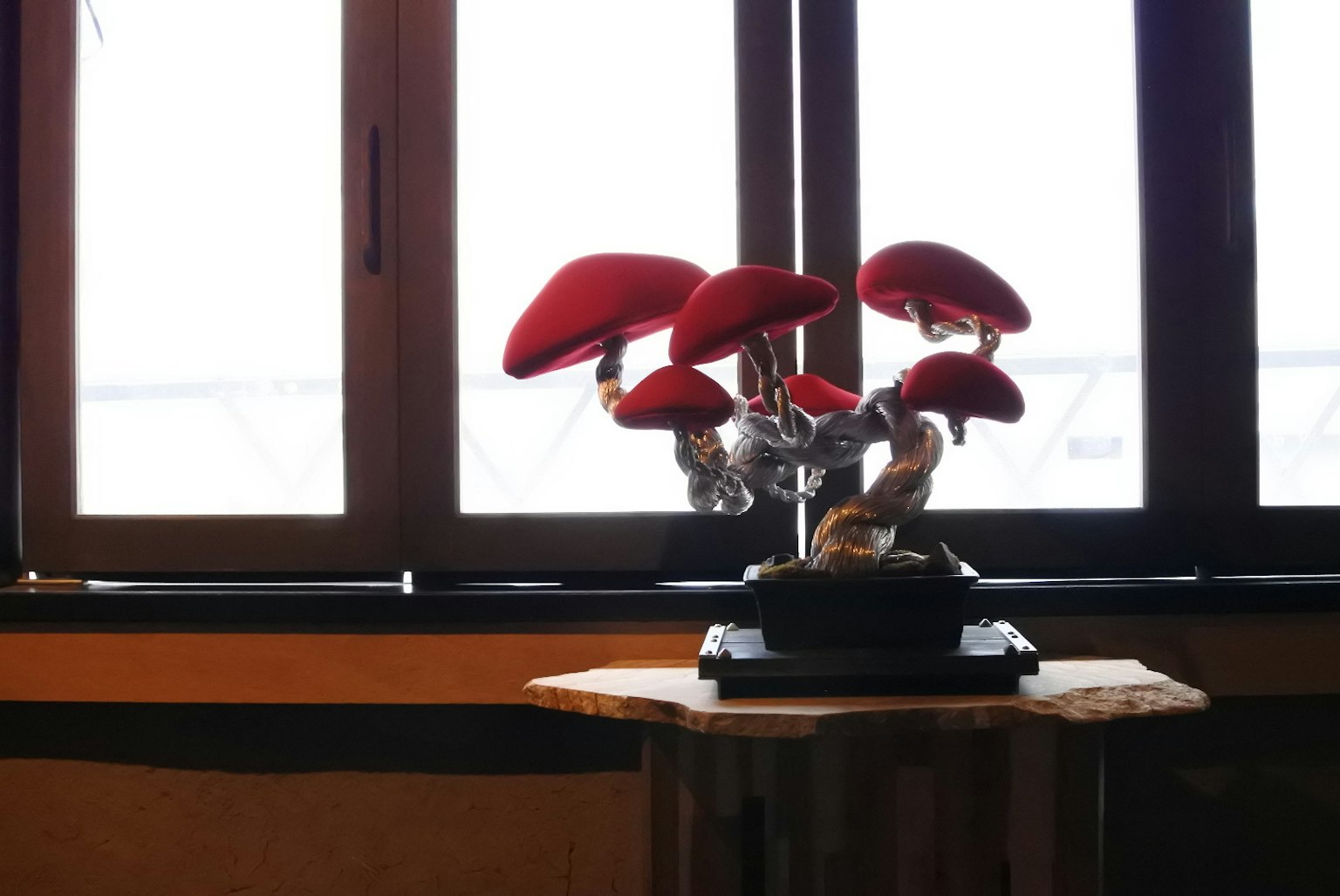 Ein Bonsai mit roten Pilzen, das an einem Fenster steht