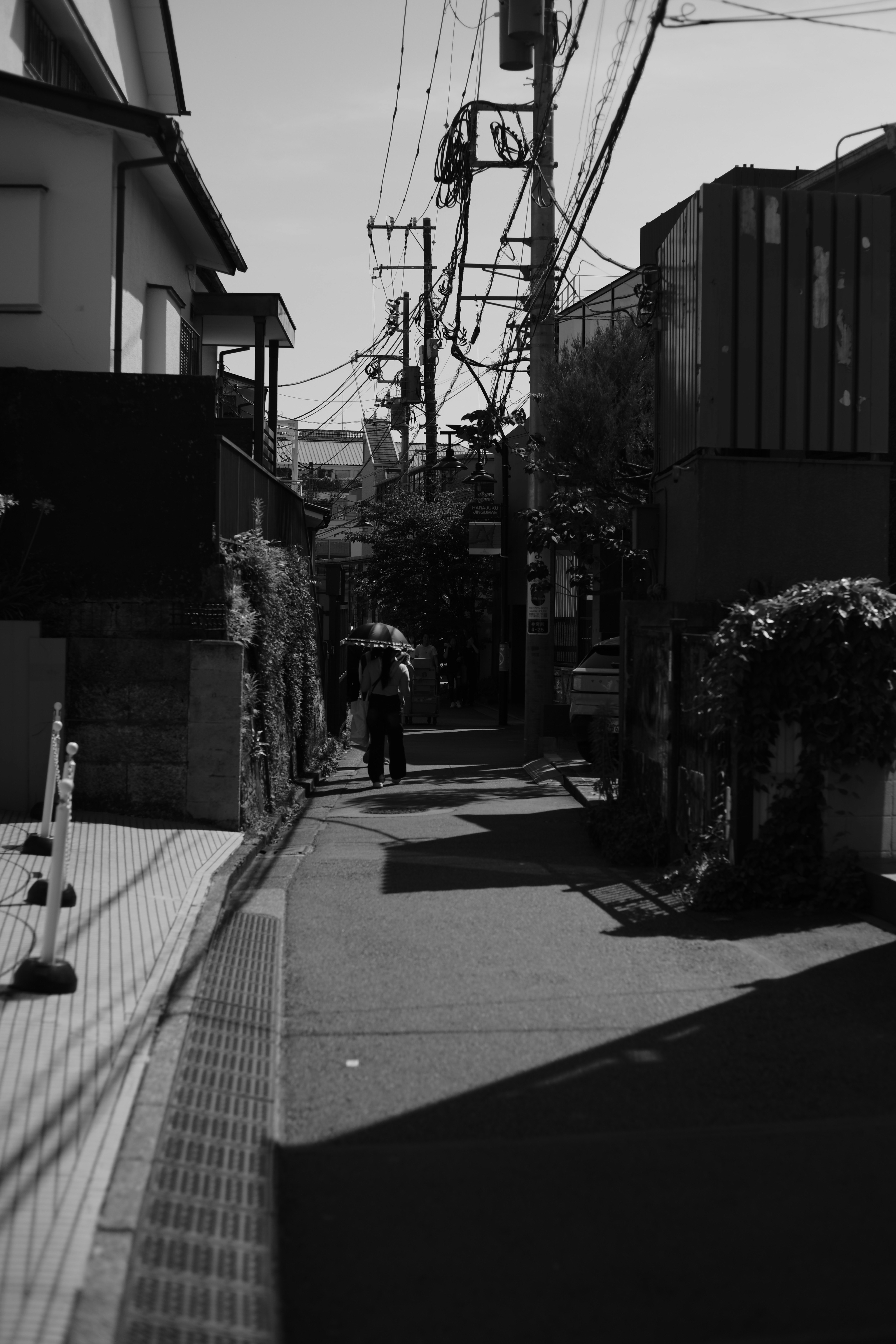 路地の奥へ歩く人物と電線のある街並み