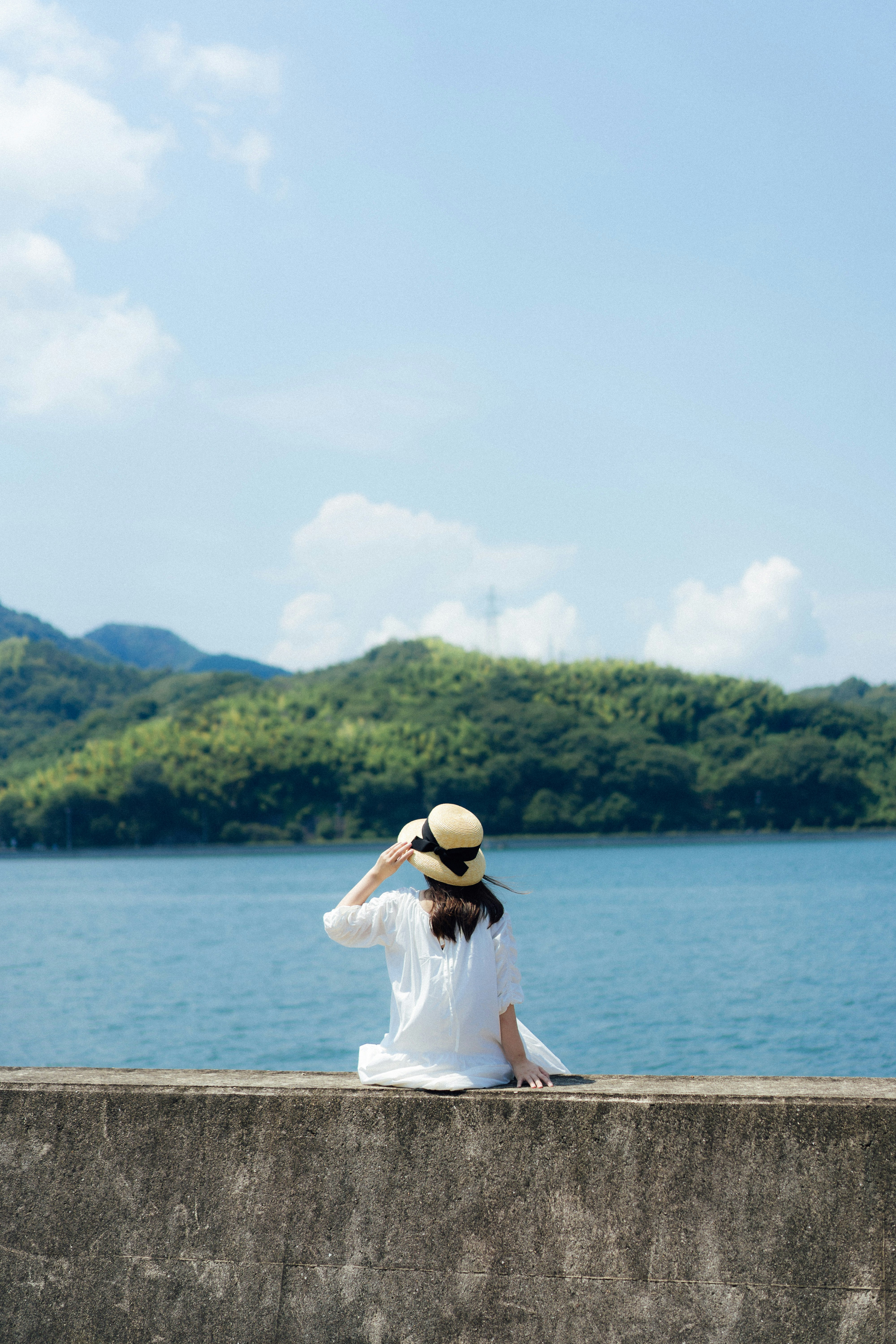 湖畔のコンクリート壁に座る麦わら帽子の人物