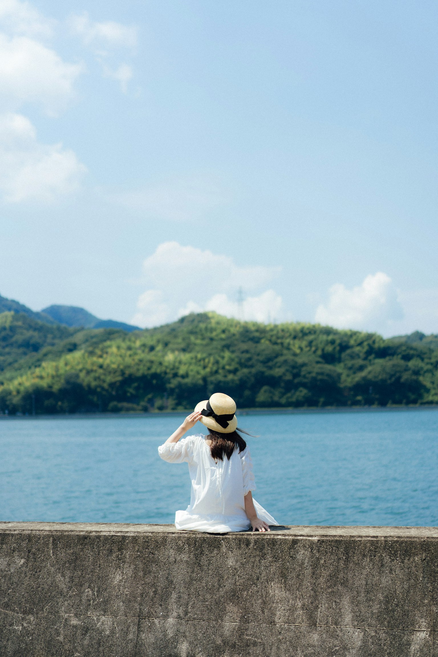 女性が海を見つめる風景 緑の山々と青い空が広がる