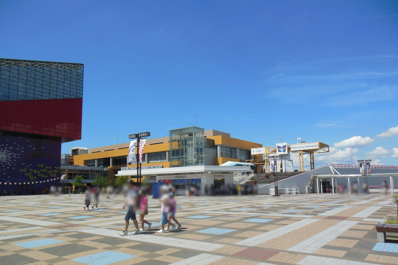People walking in a plaza under a blue sky with colorful buildings