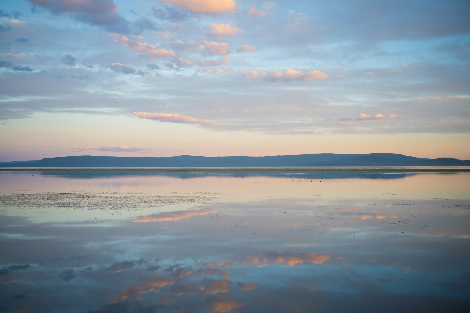 Superficie de agua tranquila reflejando el cielo y las nubes con hermosos tonos azules y naranjas
