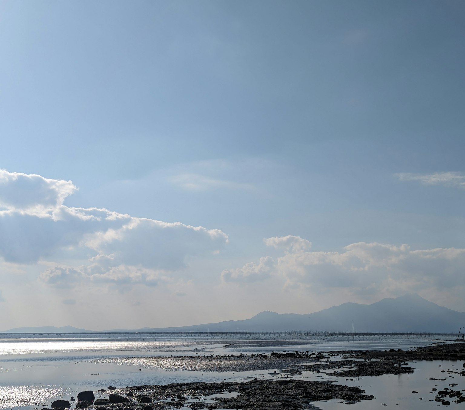 Vue panoramique d'une mer calme sous un ciel bleu avec des nuages et une côte rocheuse