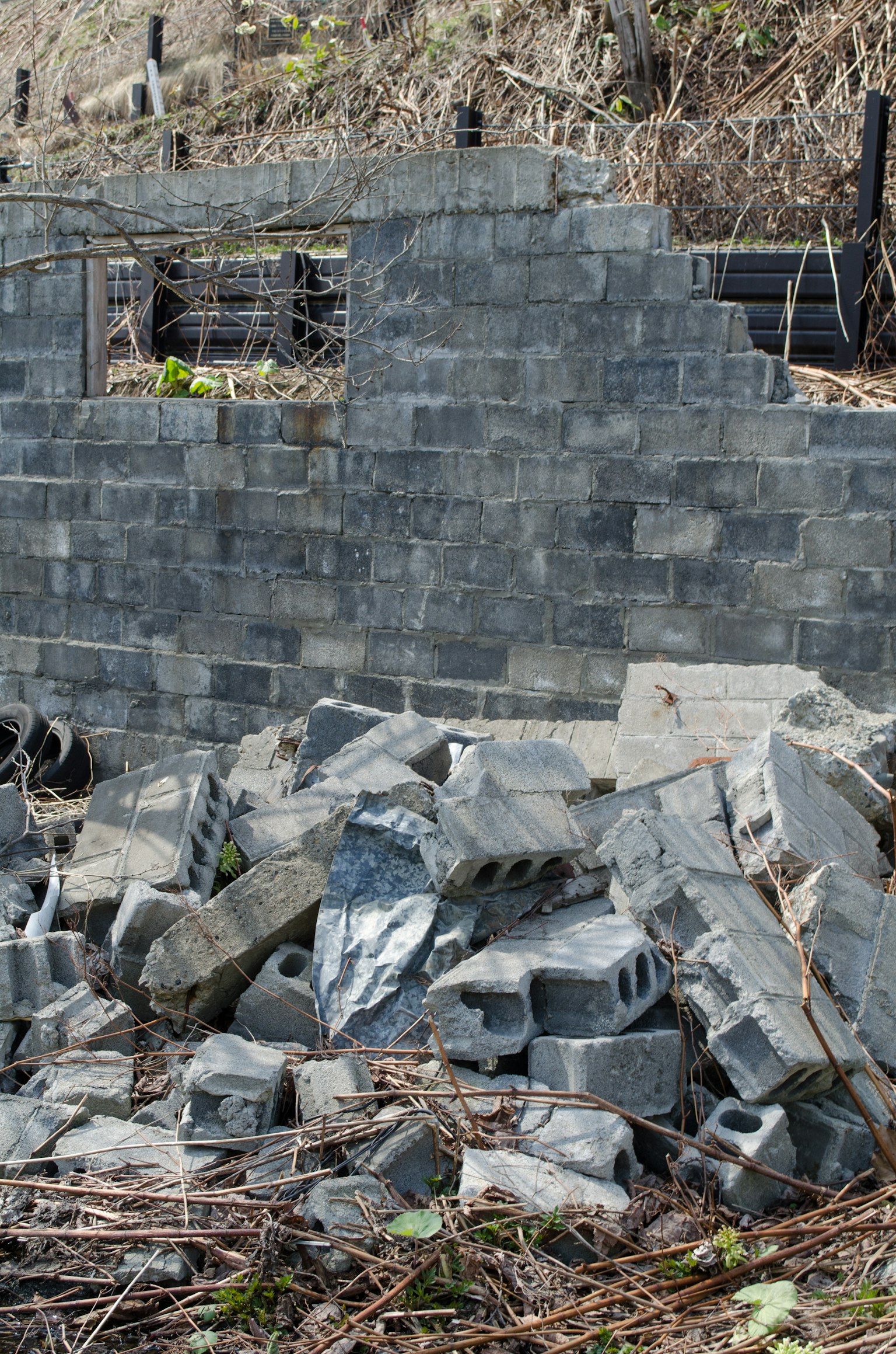Dinding blok beton yang runtuh dengan blok-blok yang berserakan di sekitarnya