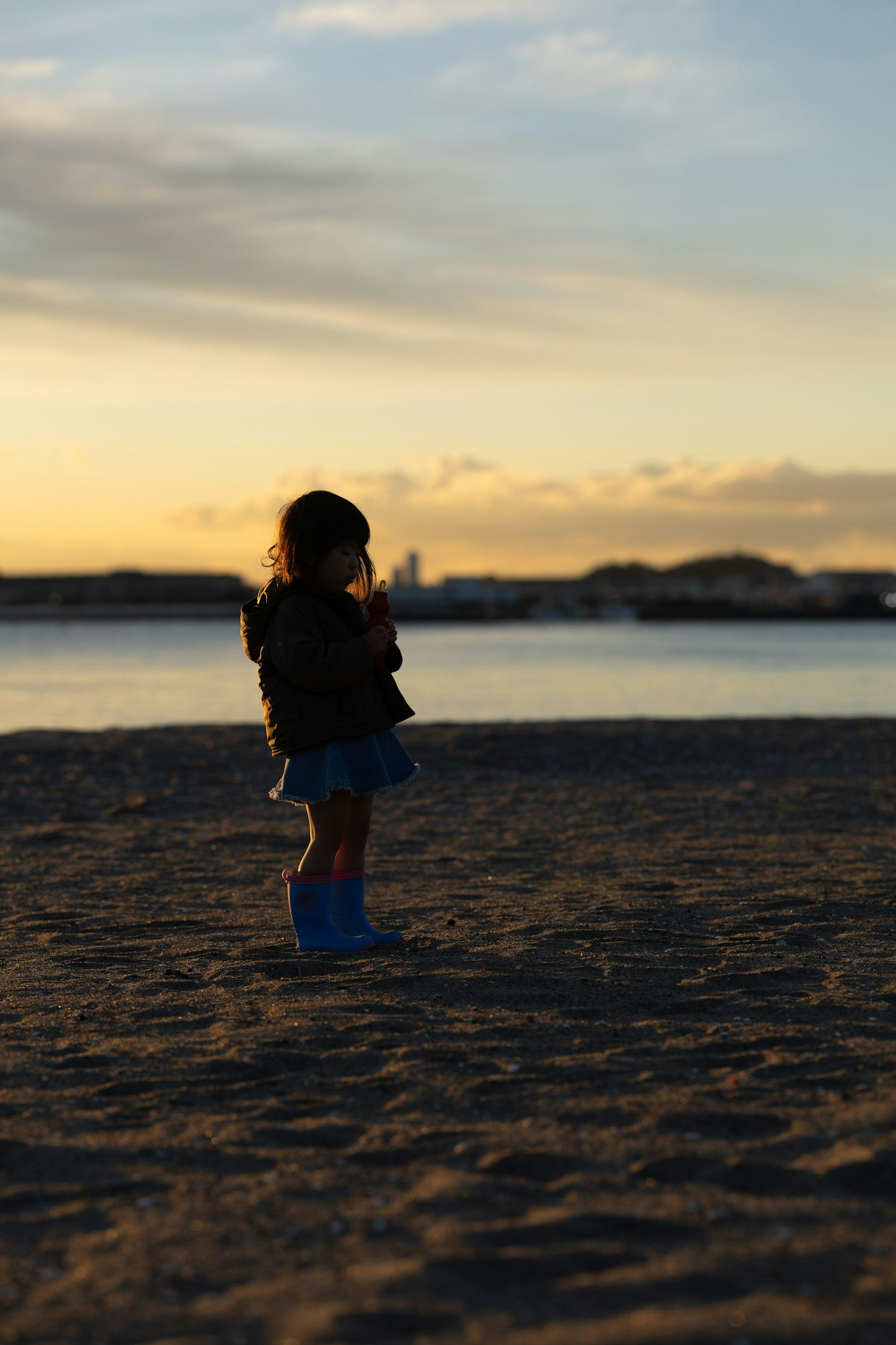 Seorang anak berdiri di pantai saat matahari terbenam