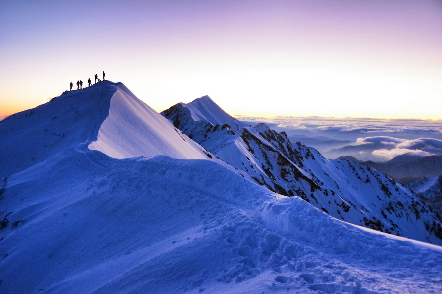 Silhouetten von Bergsteigern auf einem schneebedeckten Berggipfel mit einem schönen Sonnenaufgangshimmel
