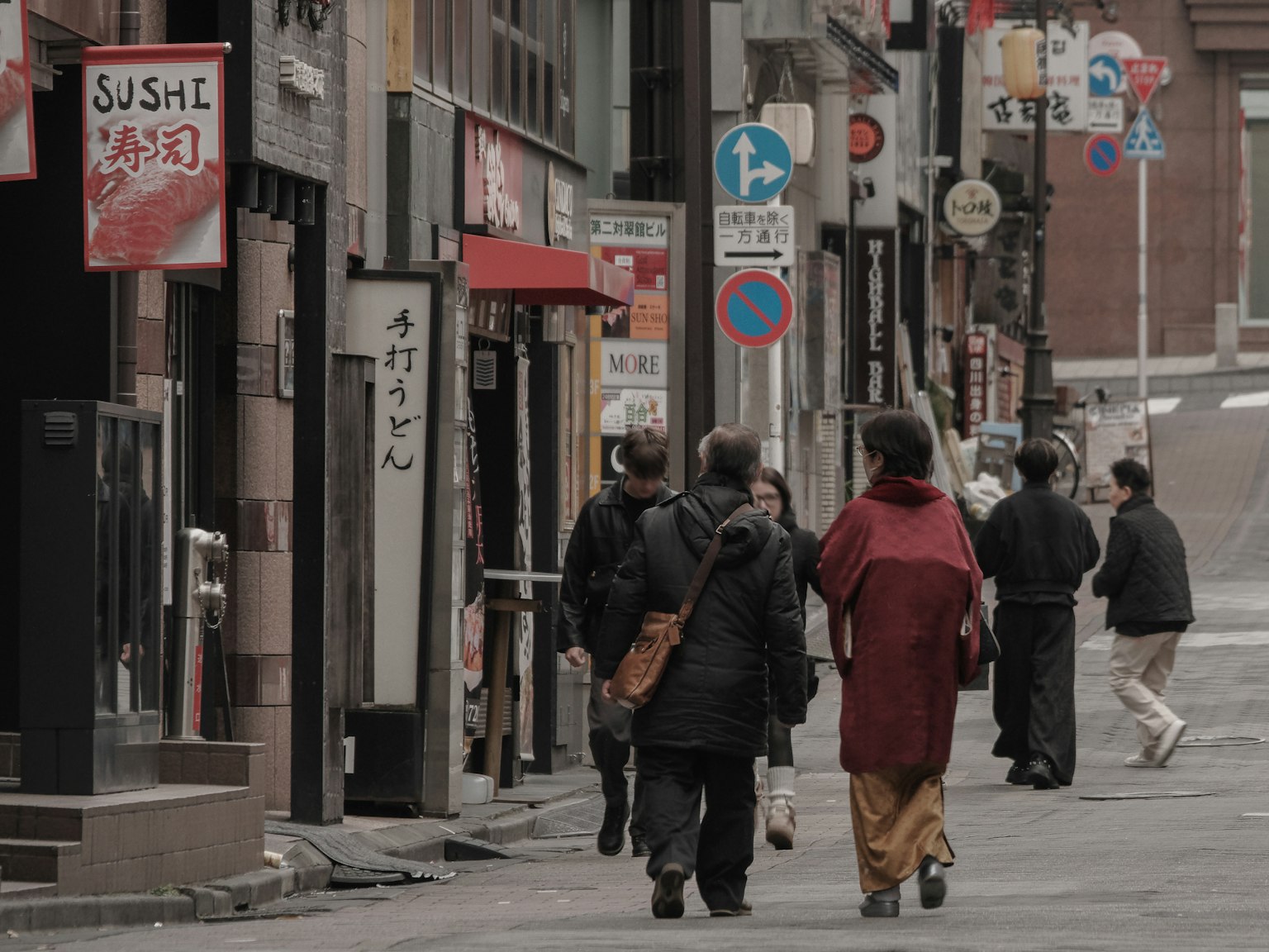 People walking in a city street featuring a woman in a kimono and individuals in black coats