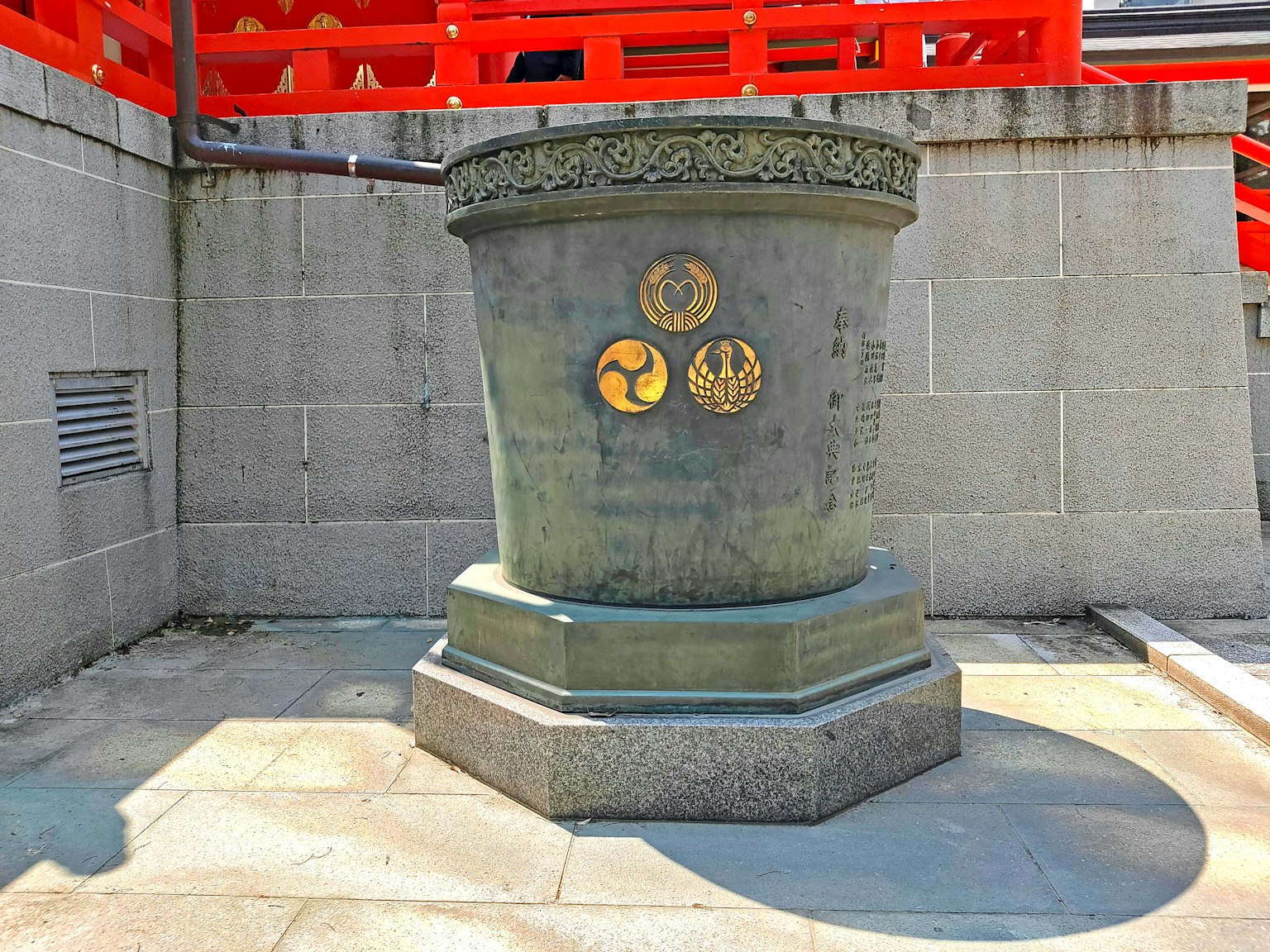 Dekorativer Steinpfeiler in der Nähe eines roten Torii mit drei goldenen Emblemen