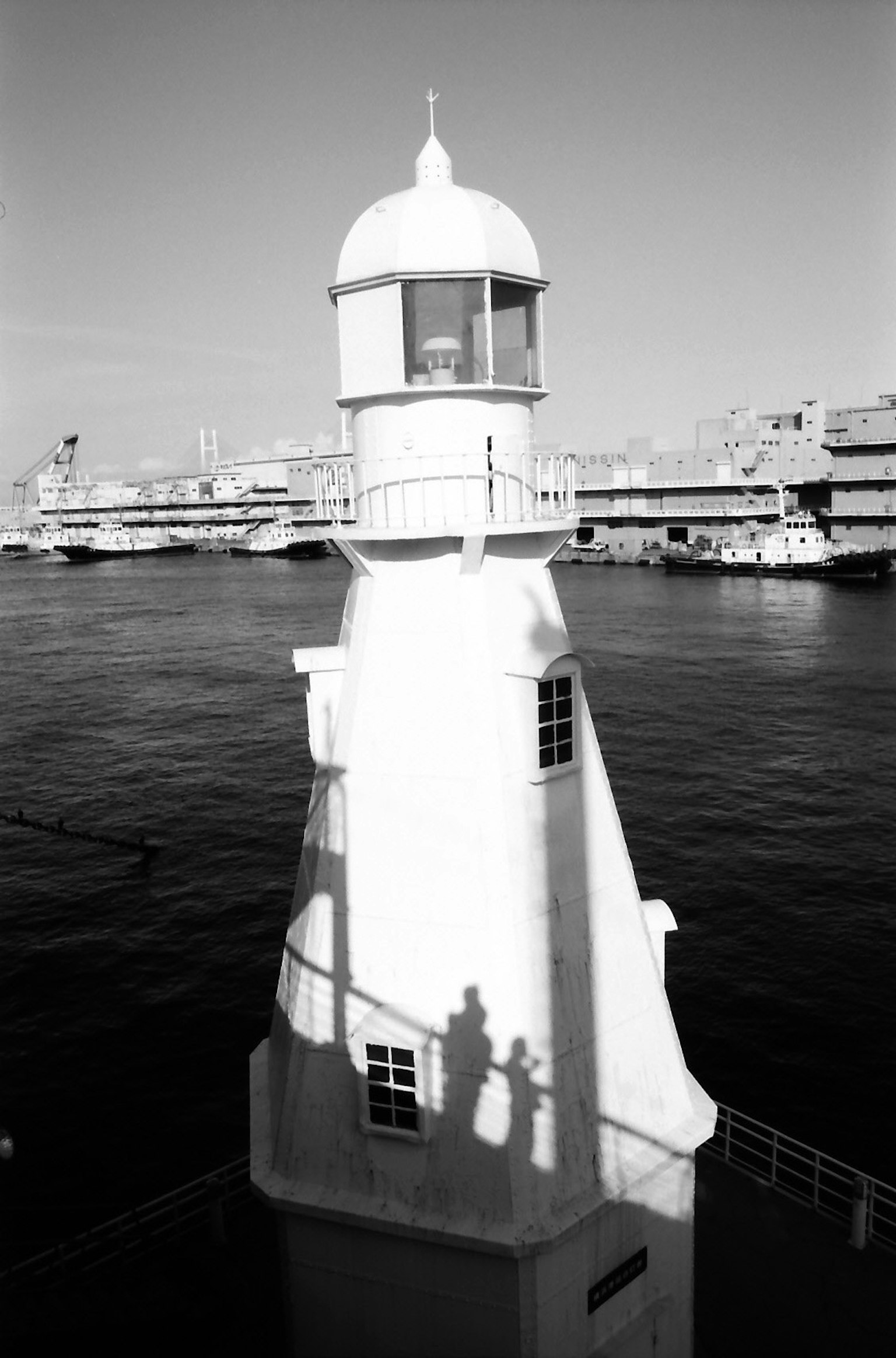 Faro in bianco e nero con ombre nel porto