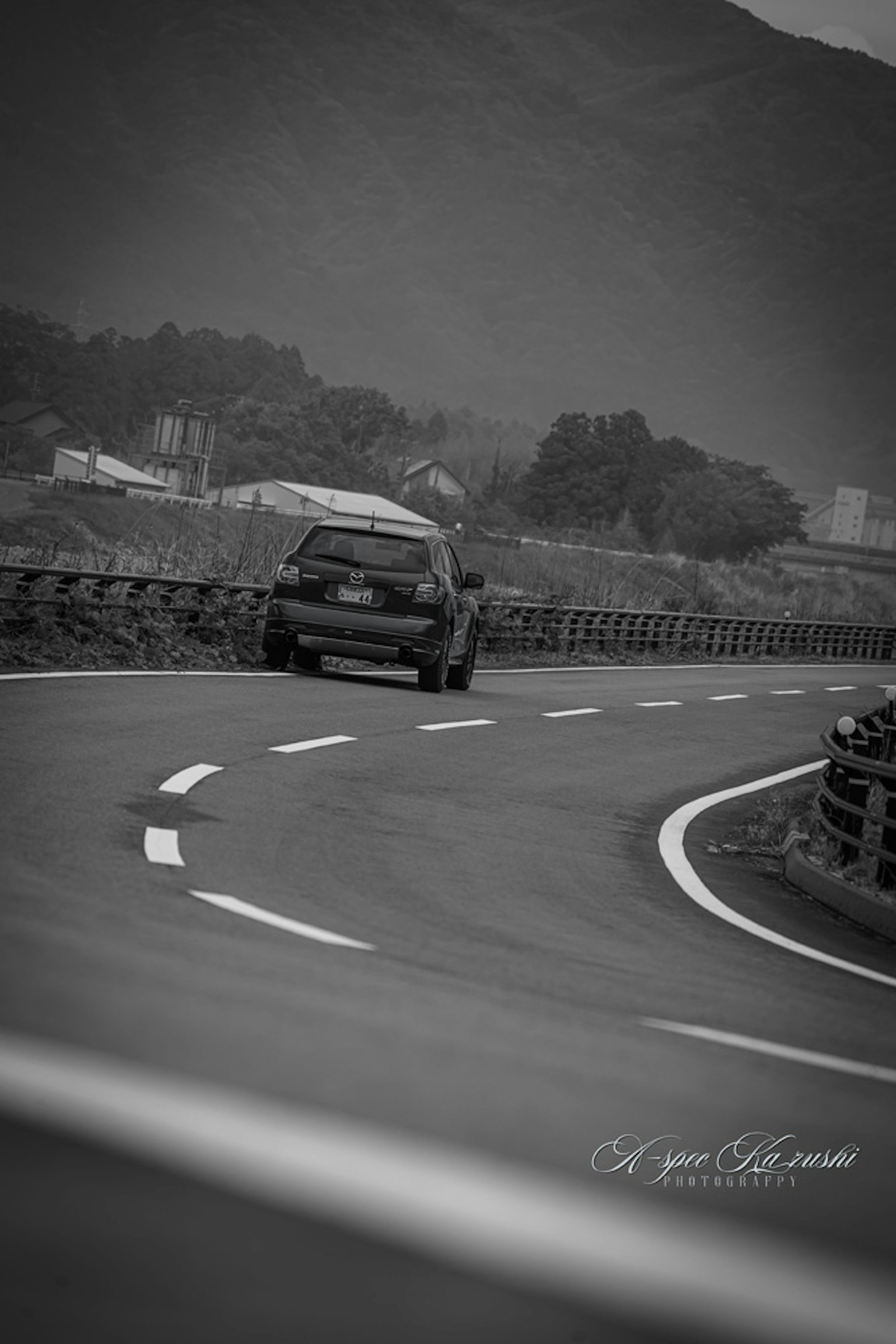 Black and white car navigating a winding road with mountains in the background