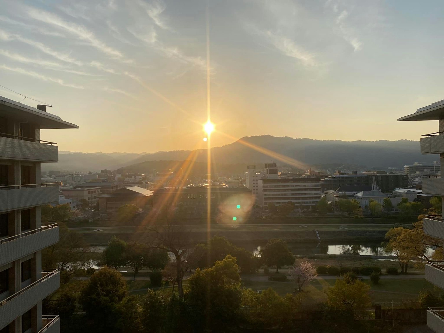 Beautiful landscape with the sun rising behind mountains buildings and a river