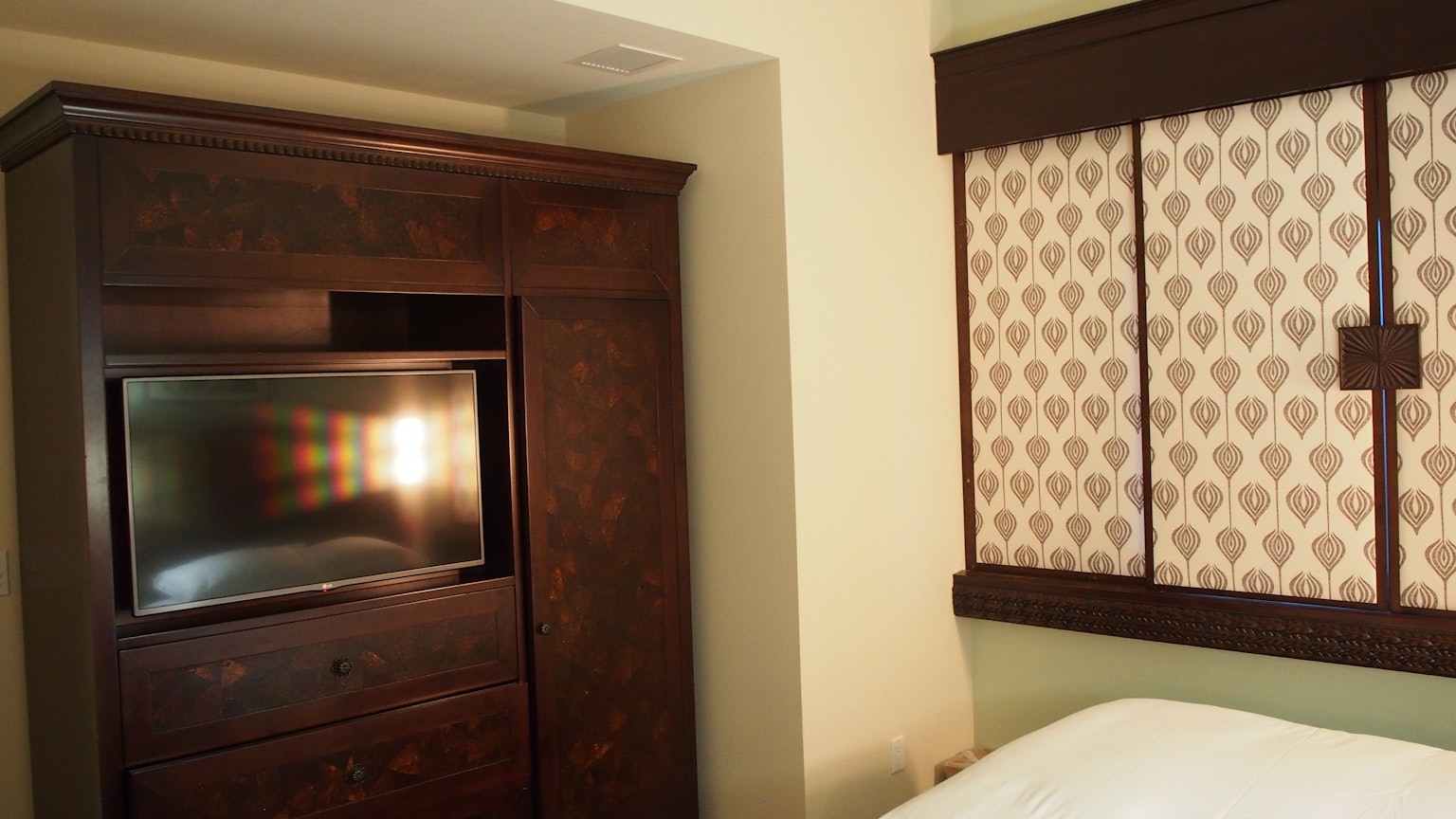 Une chambre avec un cabinet en bois sombre contenant une télévision et des rideaux décoratifs à la fenêtre