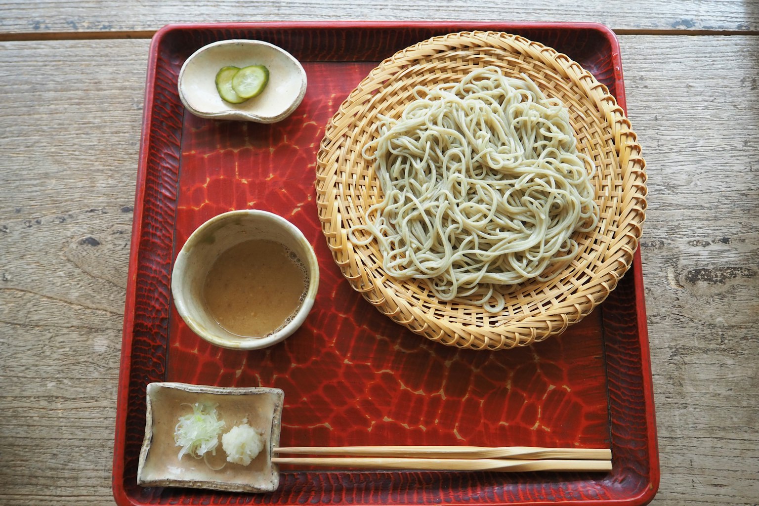 Soba-Nudeln auf einer Bambusmatte mit Dipsauce und Garnituren serviert