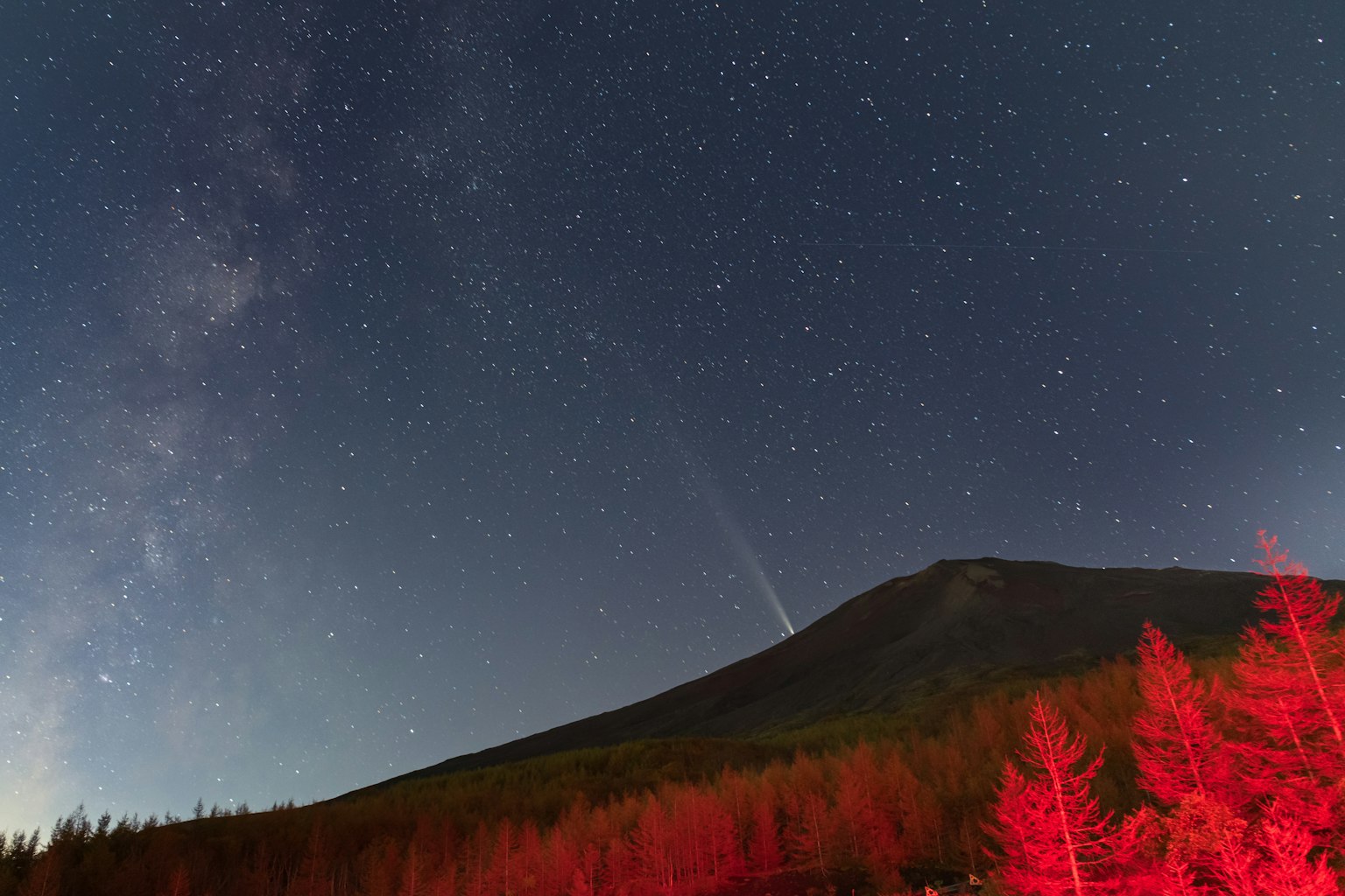 Monte Fuji bajo un cielo estrellado con árboles rojos