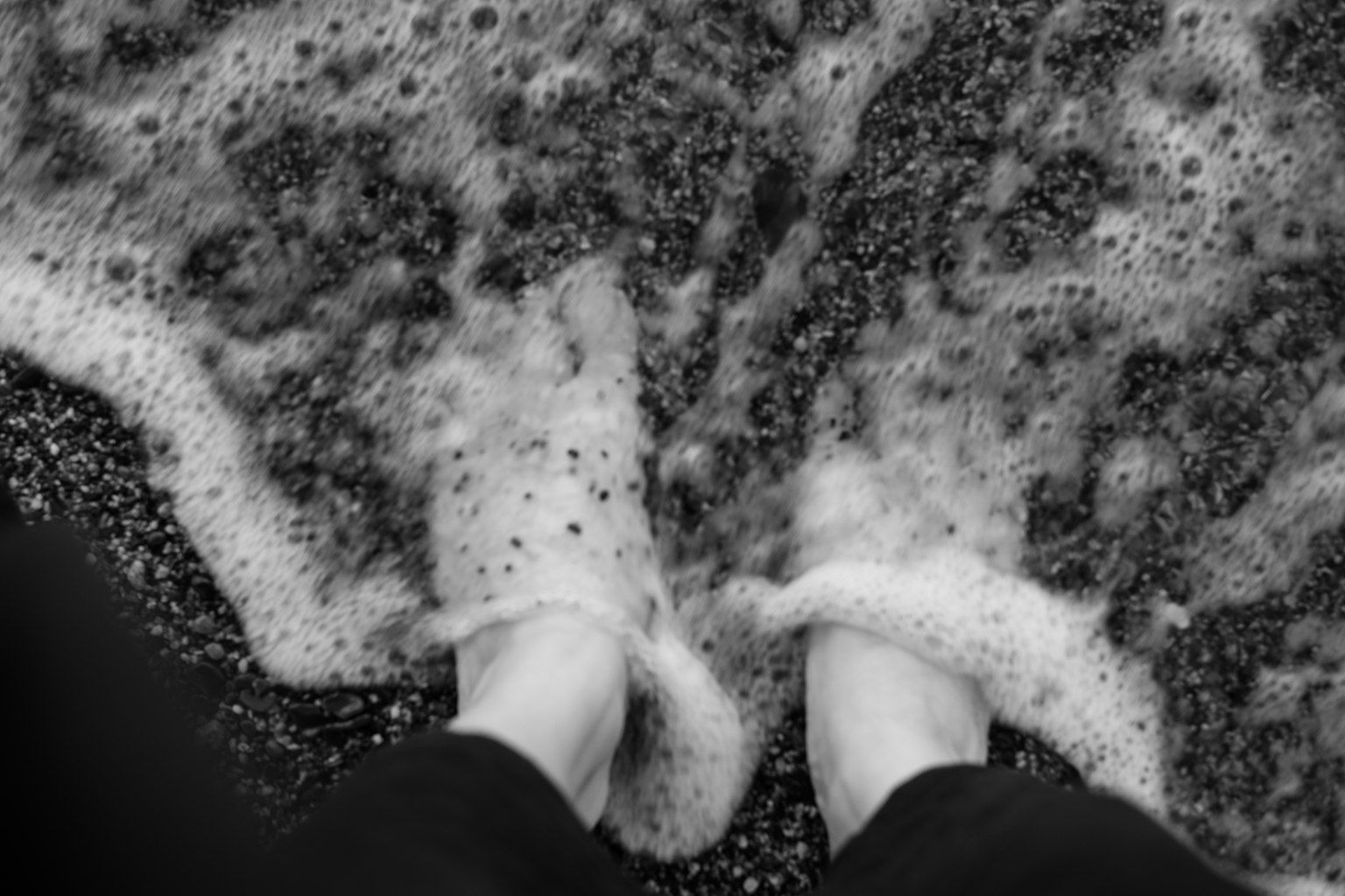 Photo en noir et blanc de pieds dans les vagues de l'océan