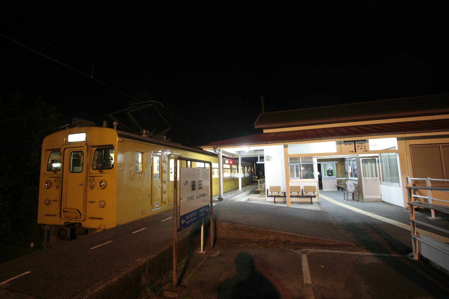 Yellow train at a rural station during the night with surrounding buildings