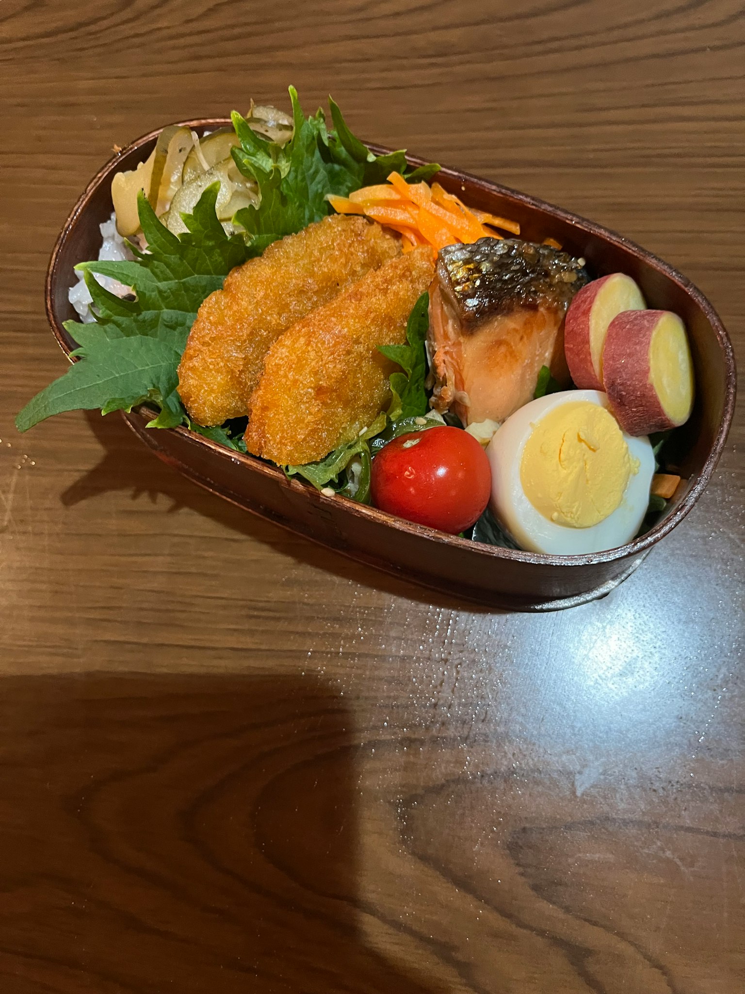 Hộp bento với salad, trứng, cà chua bi và cá chiên