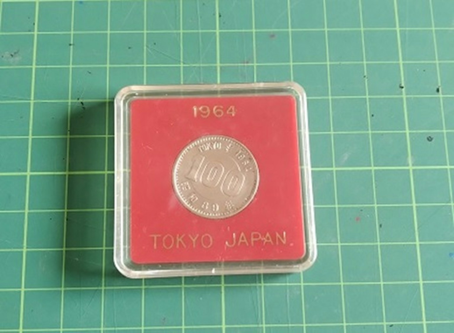 เหรียญจากโตเกียวญี่ปุ่นแสดงในกรณีป้องกันที่มีพื้นหลังสีแดง